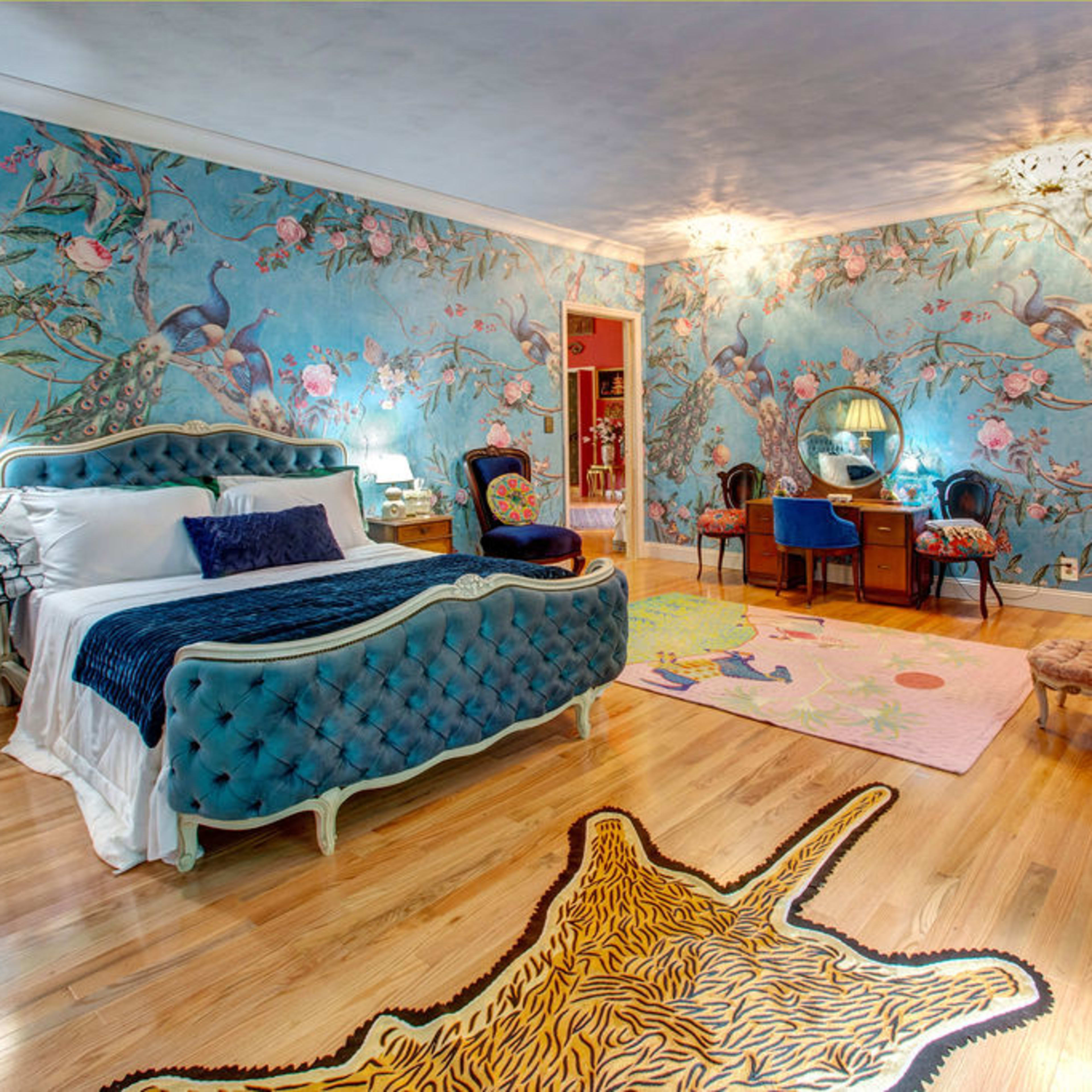 A brightly decorated bedroom featuring a blue floral wall mural, a tufted bed, an ornate dresser, and a tiger-striped rug on the wooden floor.