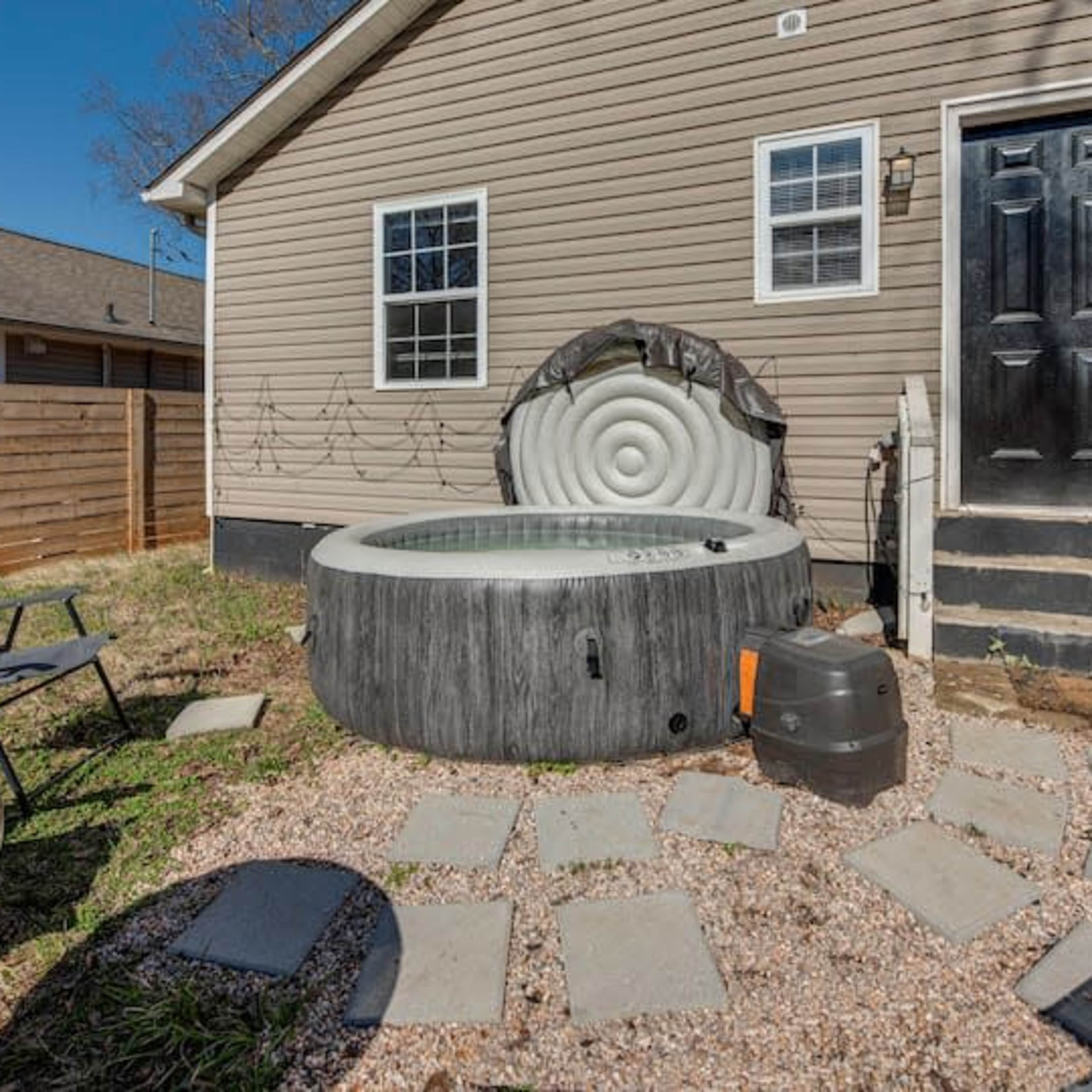 A circular hot tub on a gravel patio beside a house, with a black door and steps leading up to it.