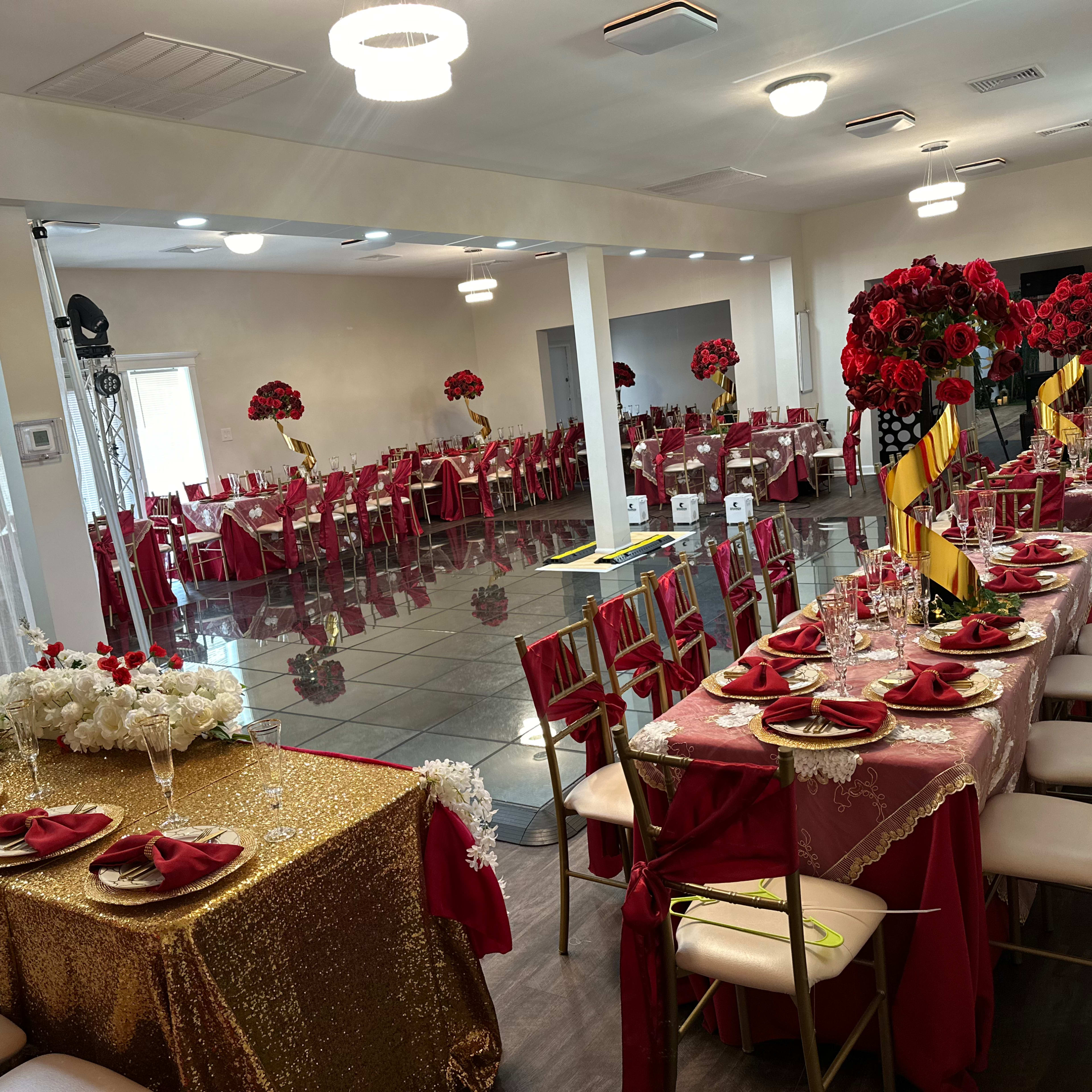 A banquet hall set up for an event, featuring red and gold tablecloths, floral centerpieces, and large floral arrangements.
