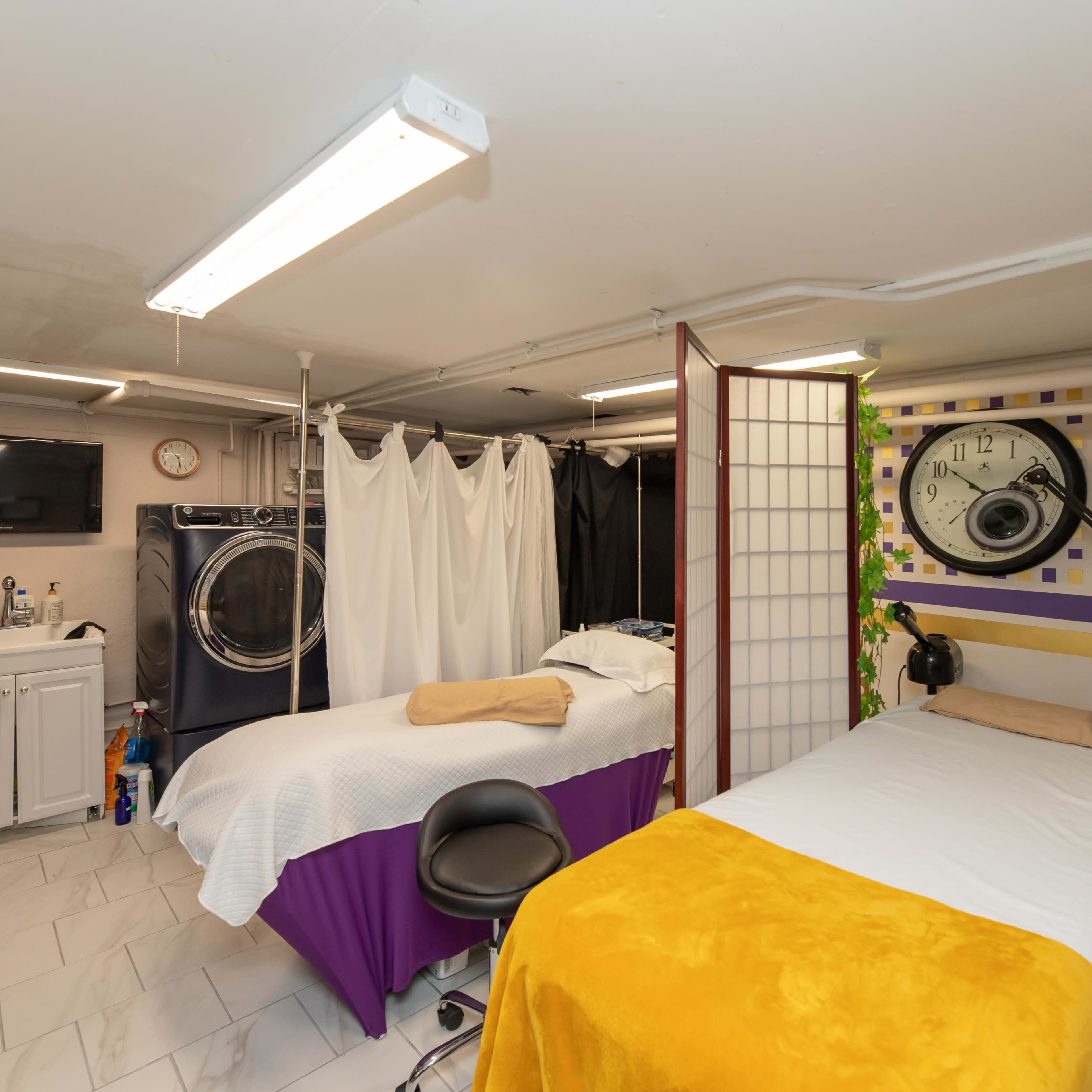 A treatment room in a basement featuring two massage tables, a washing machine, and various treatment equipment.
