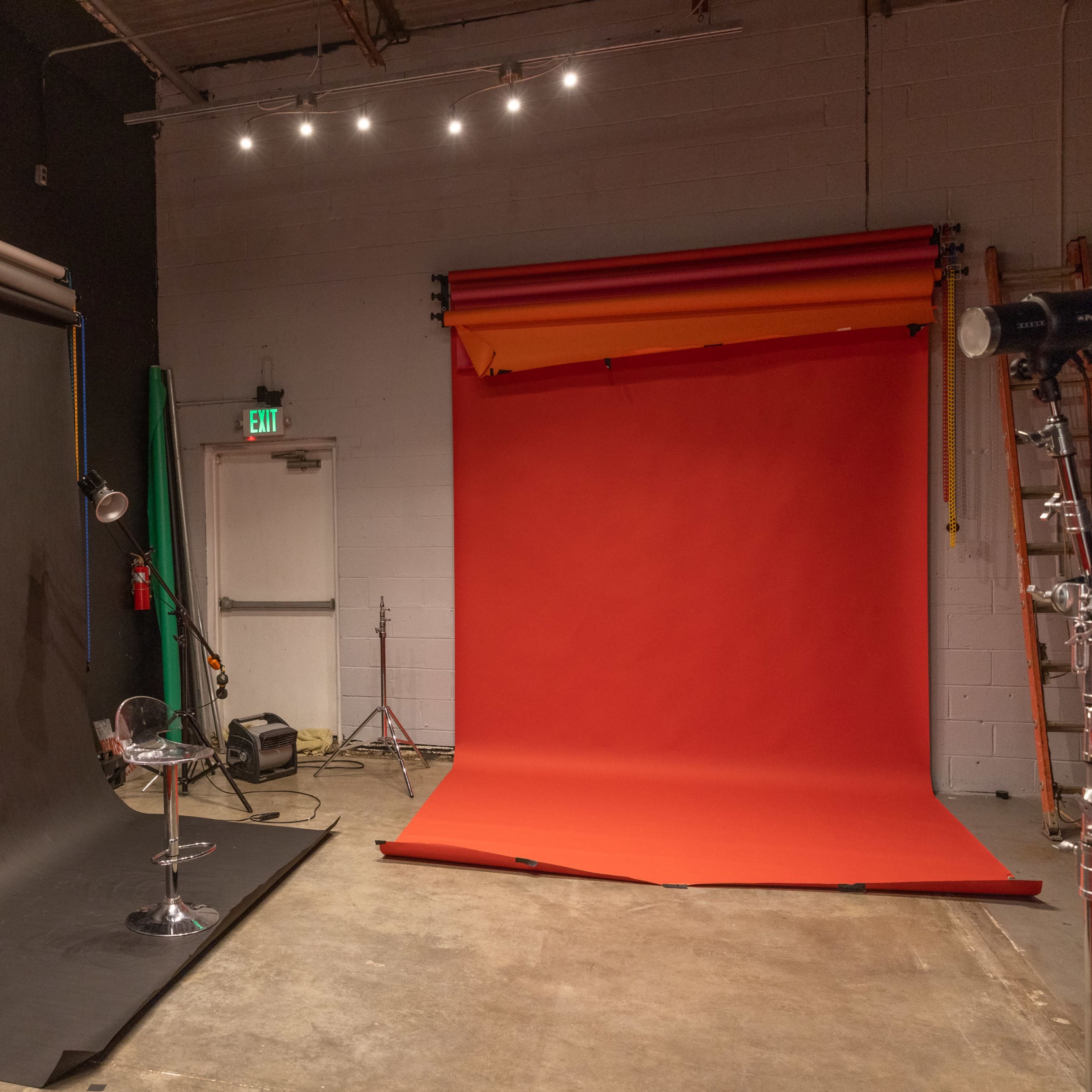 A photography studio with two backdrops, one black and one red, along with lighting equipment and a chair on the left side.