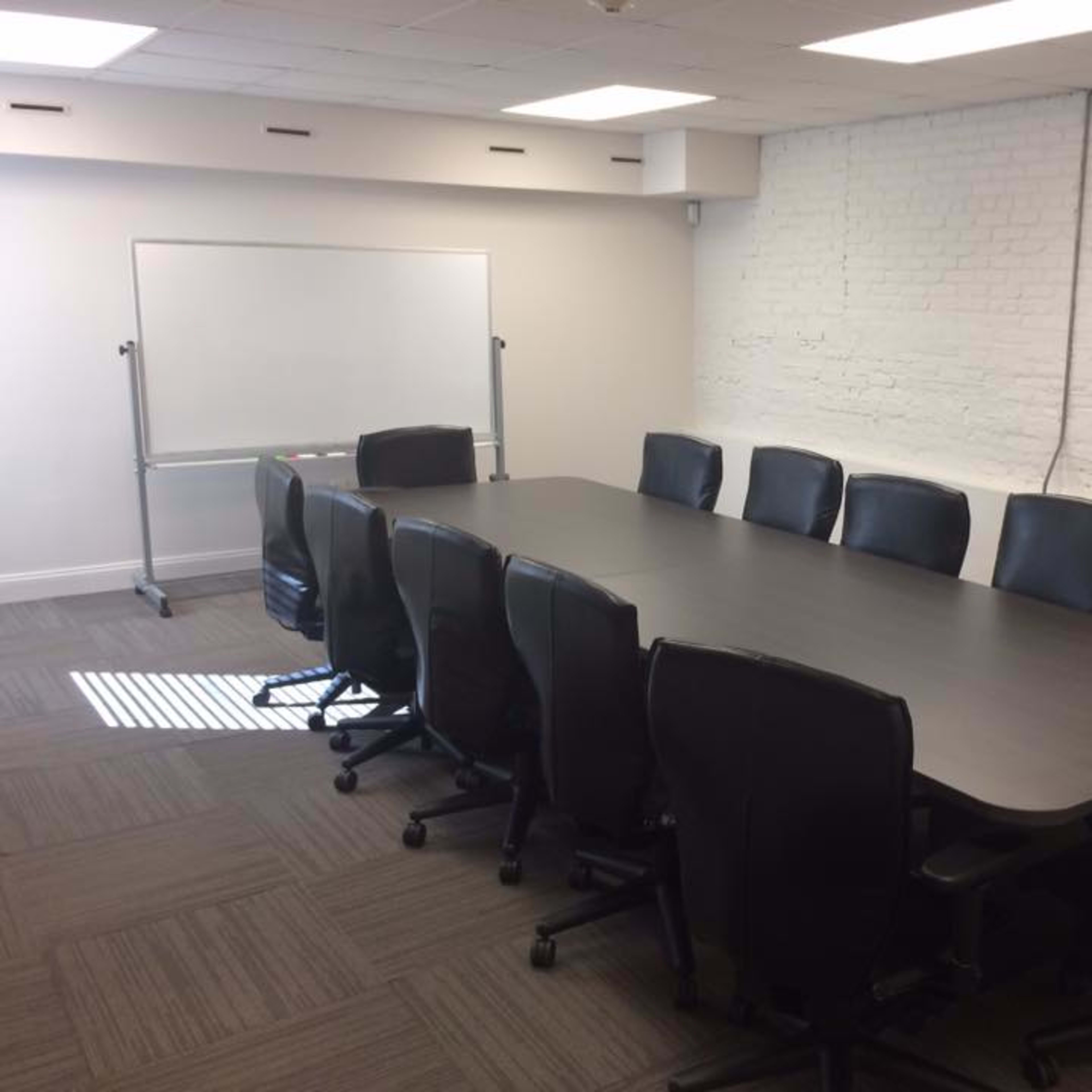 A conference room with a long, rectangular table surrounded by ten ergonomic black chairs and a whiteboard on a wall.