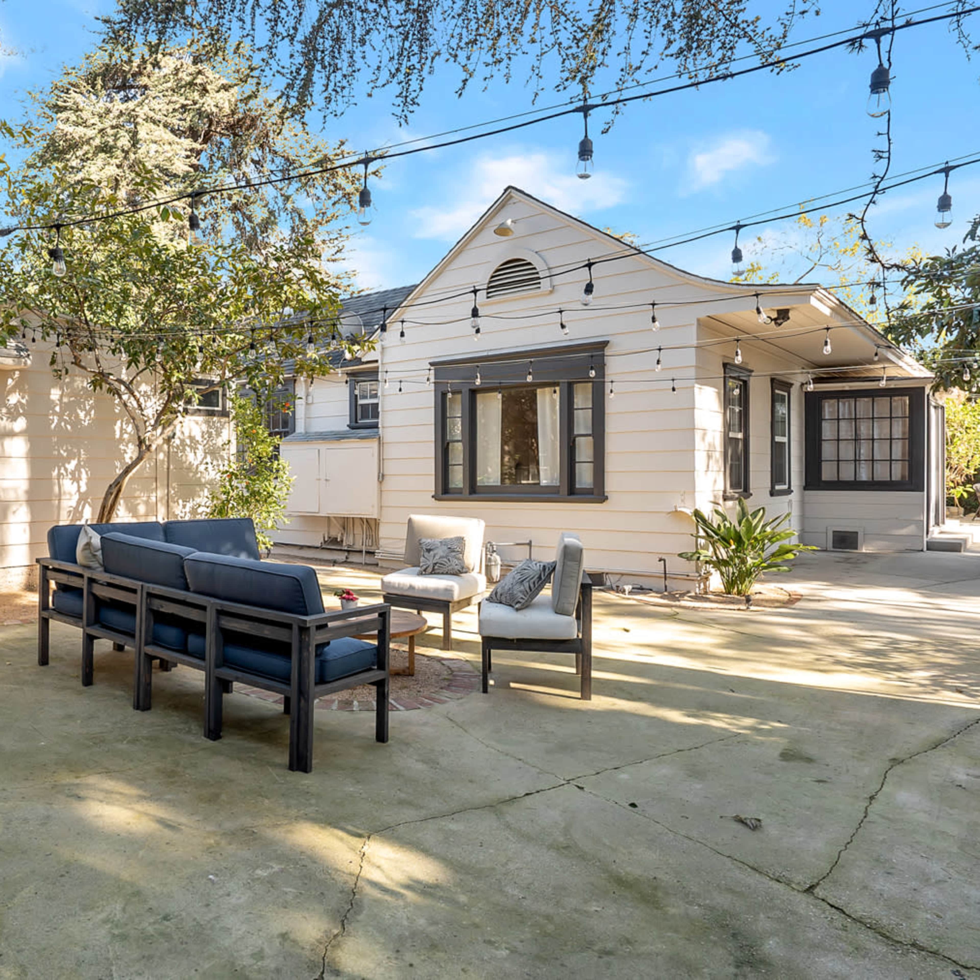 A patio area features outdoor seating and string lights, with a house and garden surrounding it.