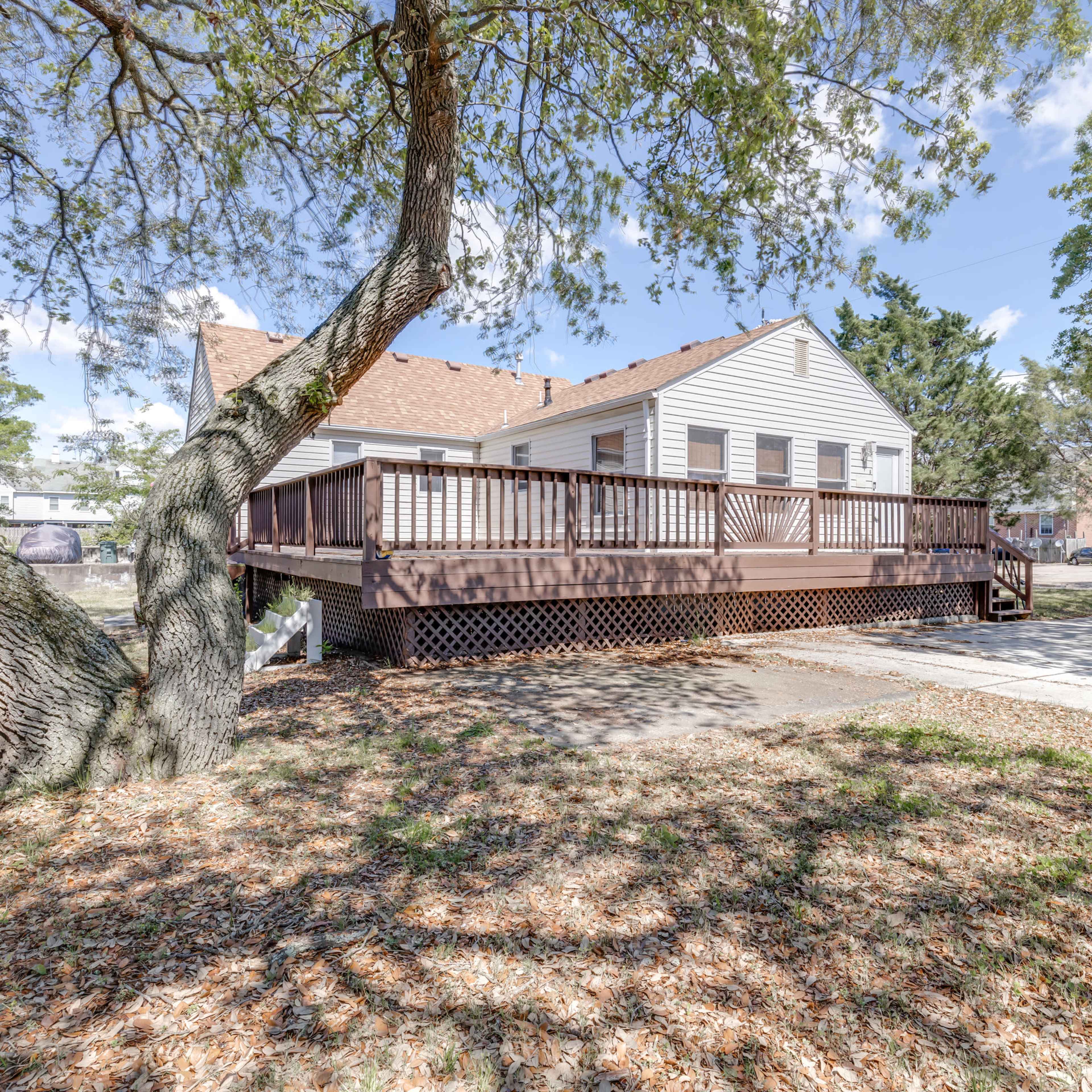 A single-story house with a large wooden deck surrounded by trees and a clear sky.