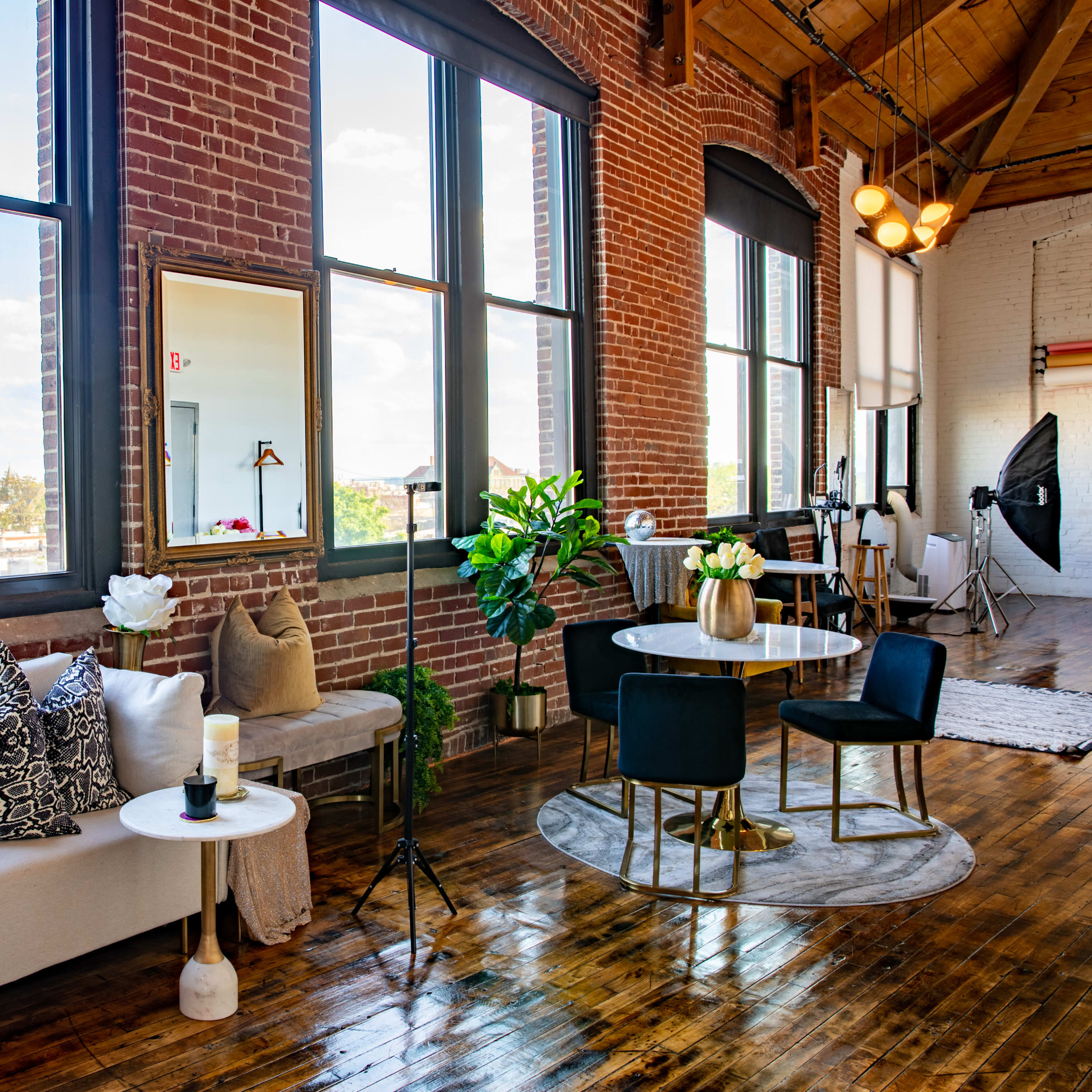 A modern loft living space with large windows, a couch, a dining table, and decorative plants.