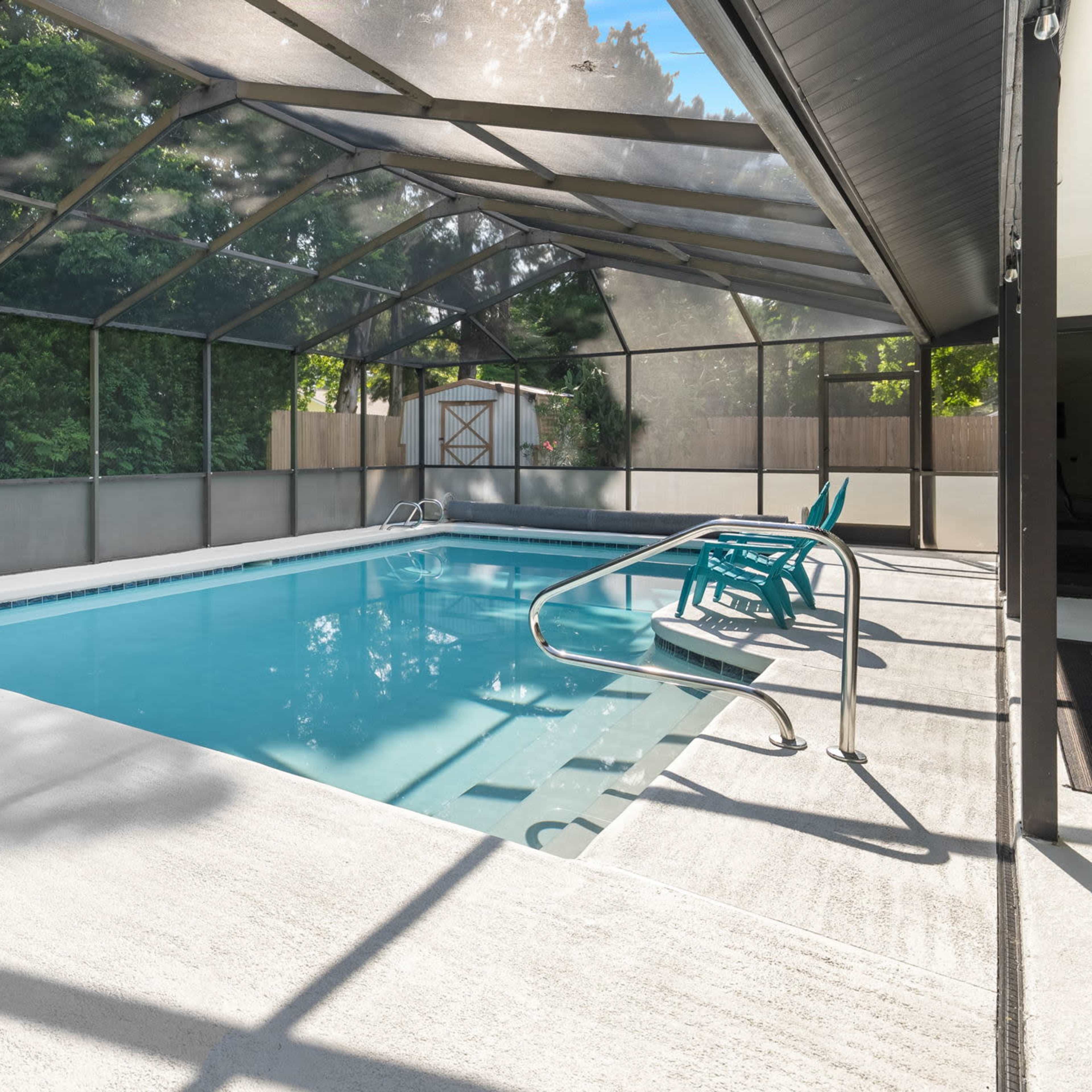 A screened-in indoor pool area with turquoise lounge chairs and a clear blue pool.