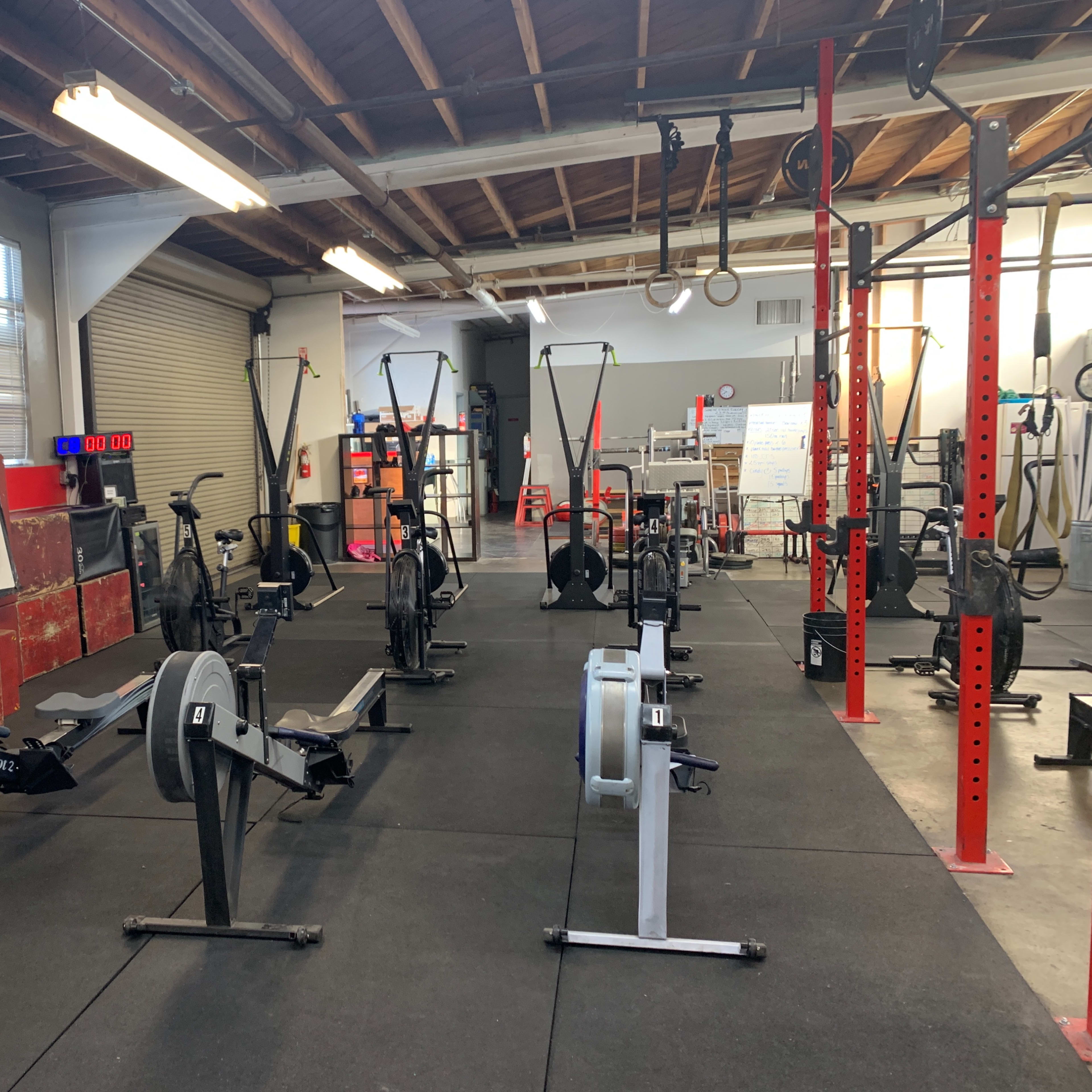A spacious gym area equipped with several rowing machines and exercise equipment, along with a whiteboard and fitness-related gear in the background.
