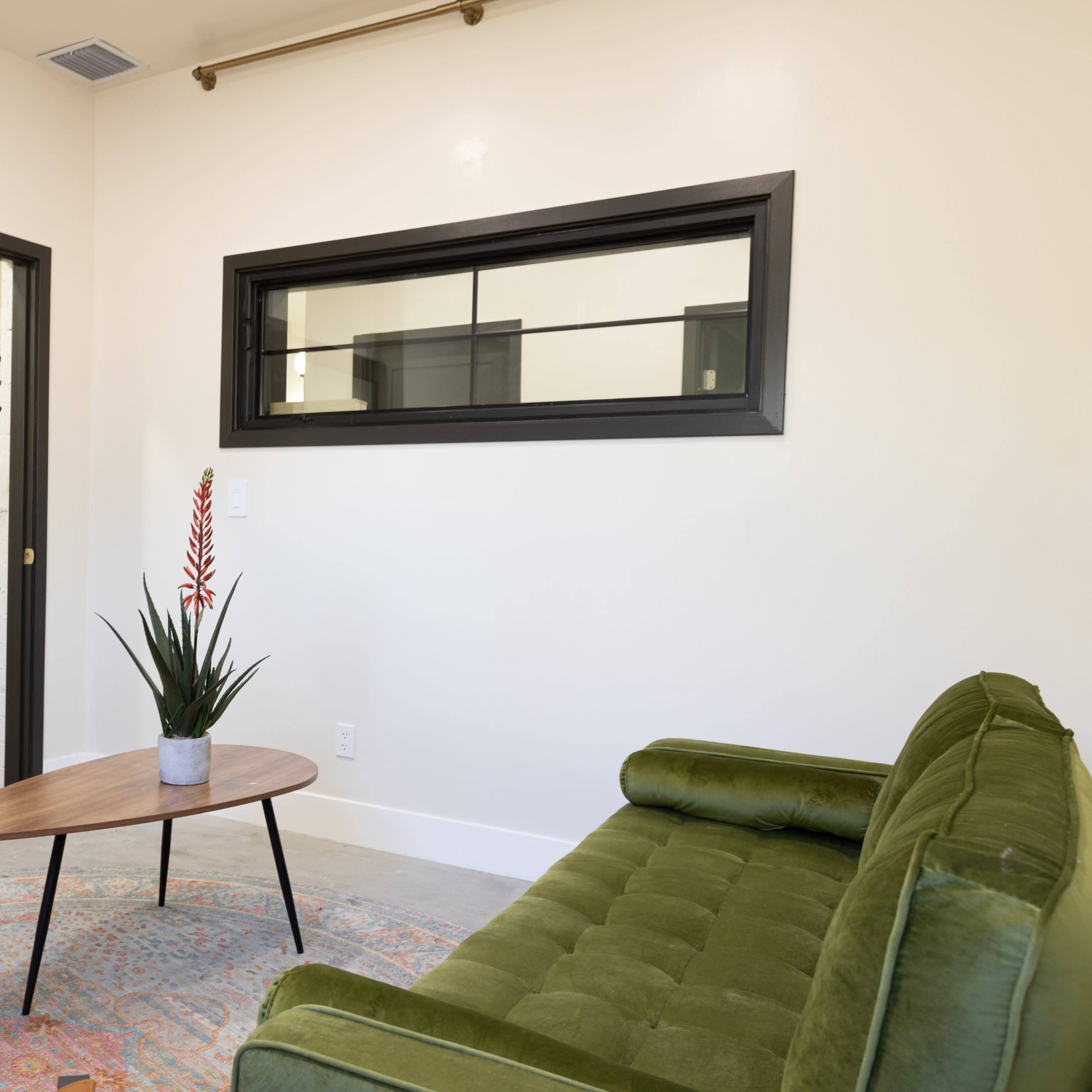 A modern room featuring a green sofa, a round coffee table, and a potted plant, with a door and a window in the background.