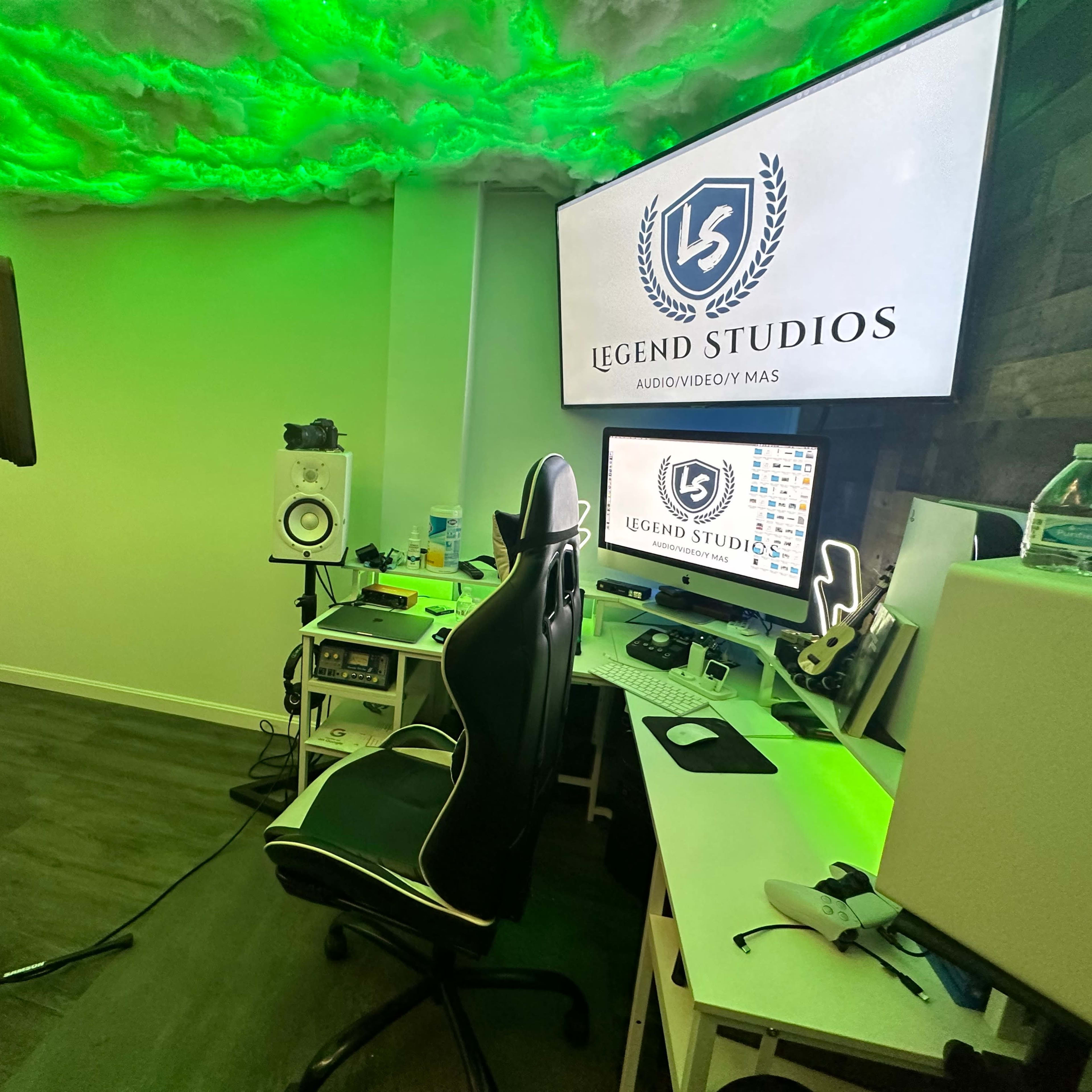 A music studio setup with a microphone, computer, and sound equipment under a green-lit ceiling.