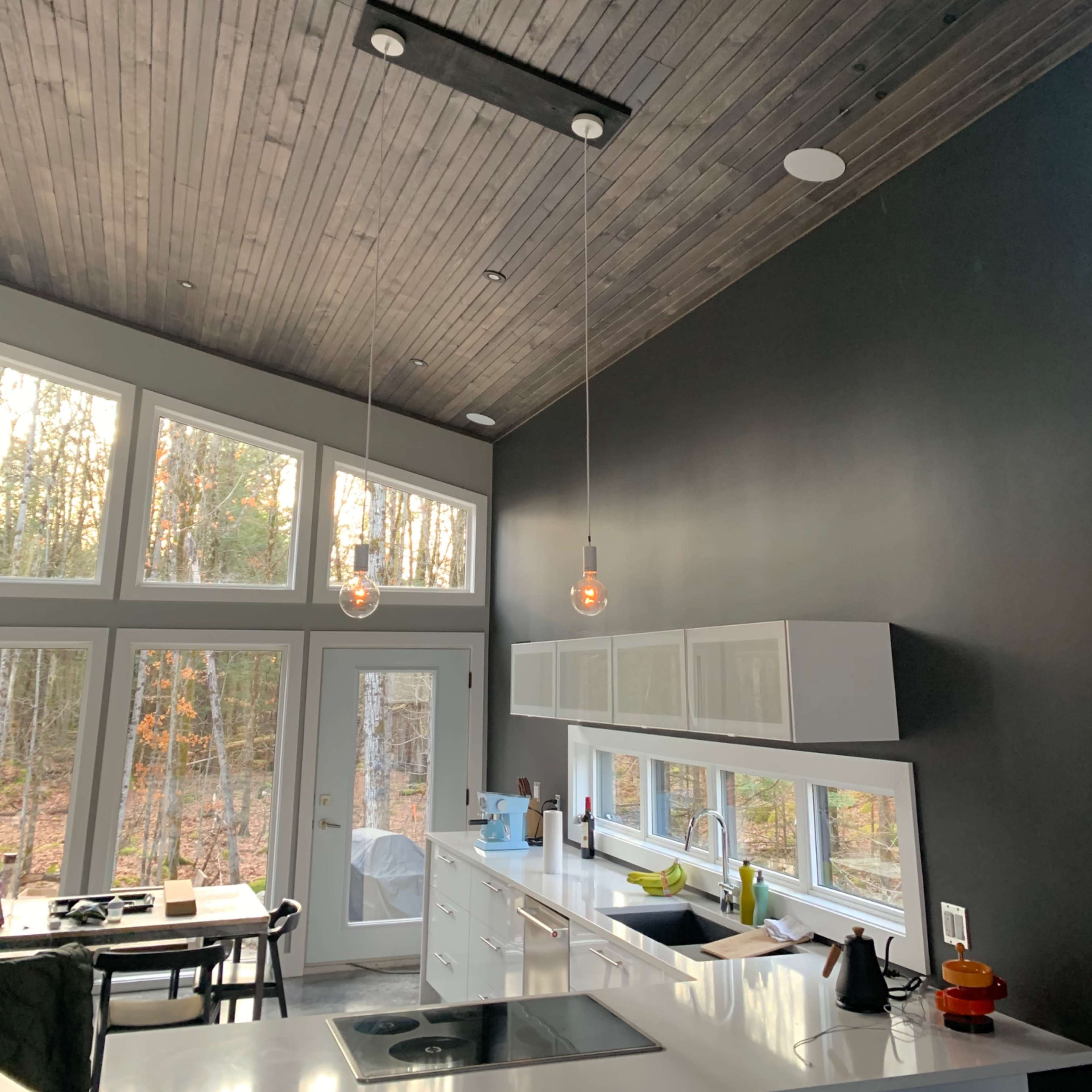 A modern kitchen with a wooden ceiling, large windows, and minimalist cabinetry.