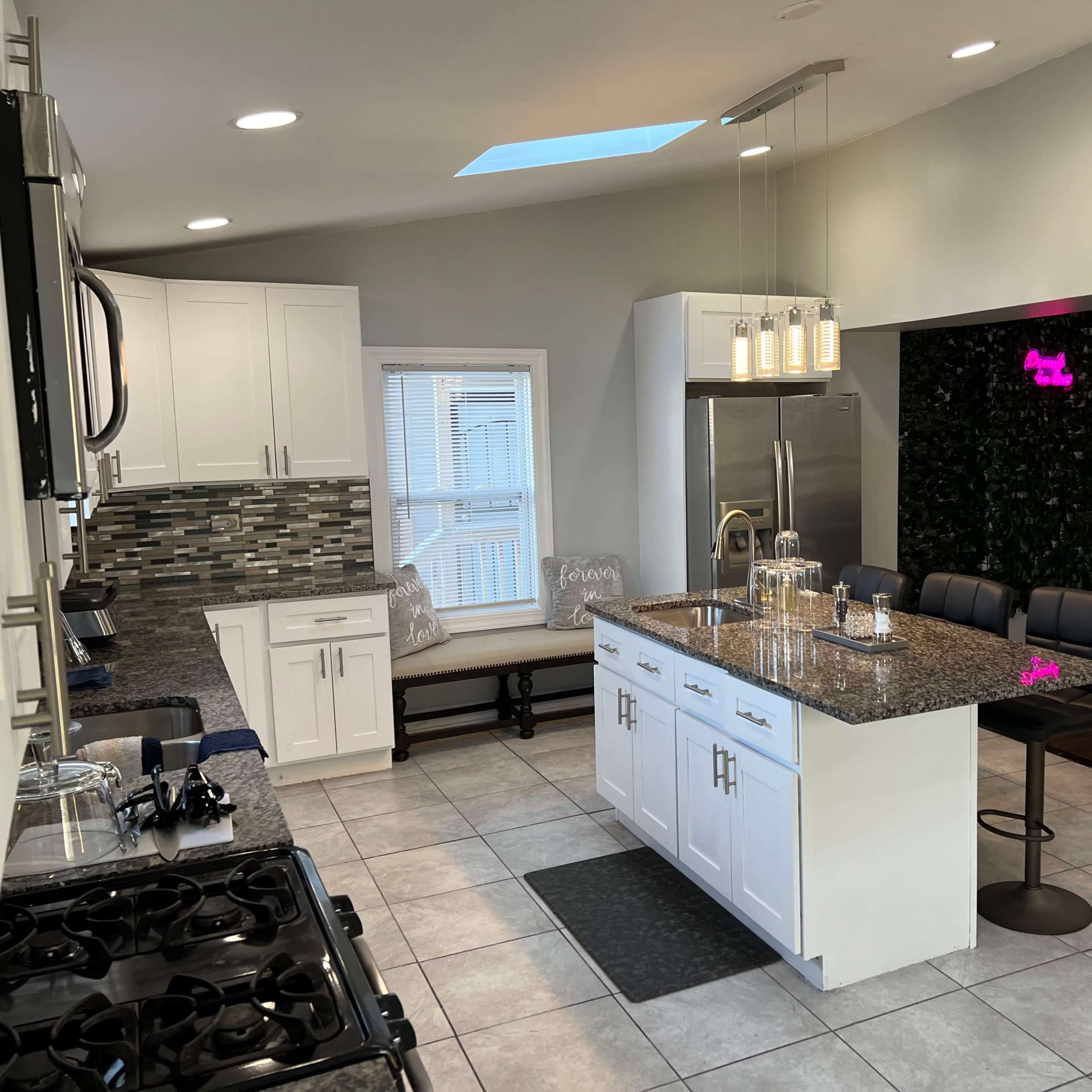 A modern kitchen features white cabinetry, a large island with seating, and a dining nook by the window.