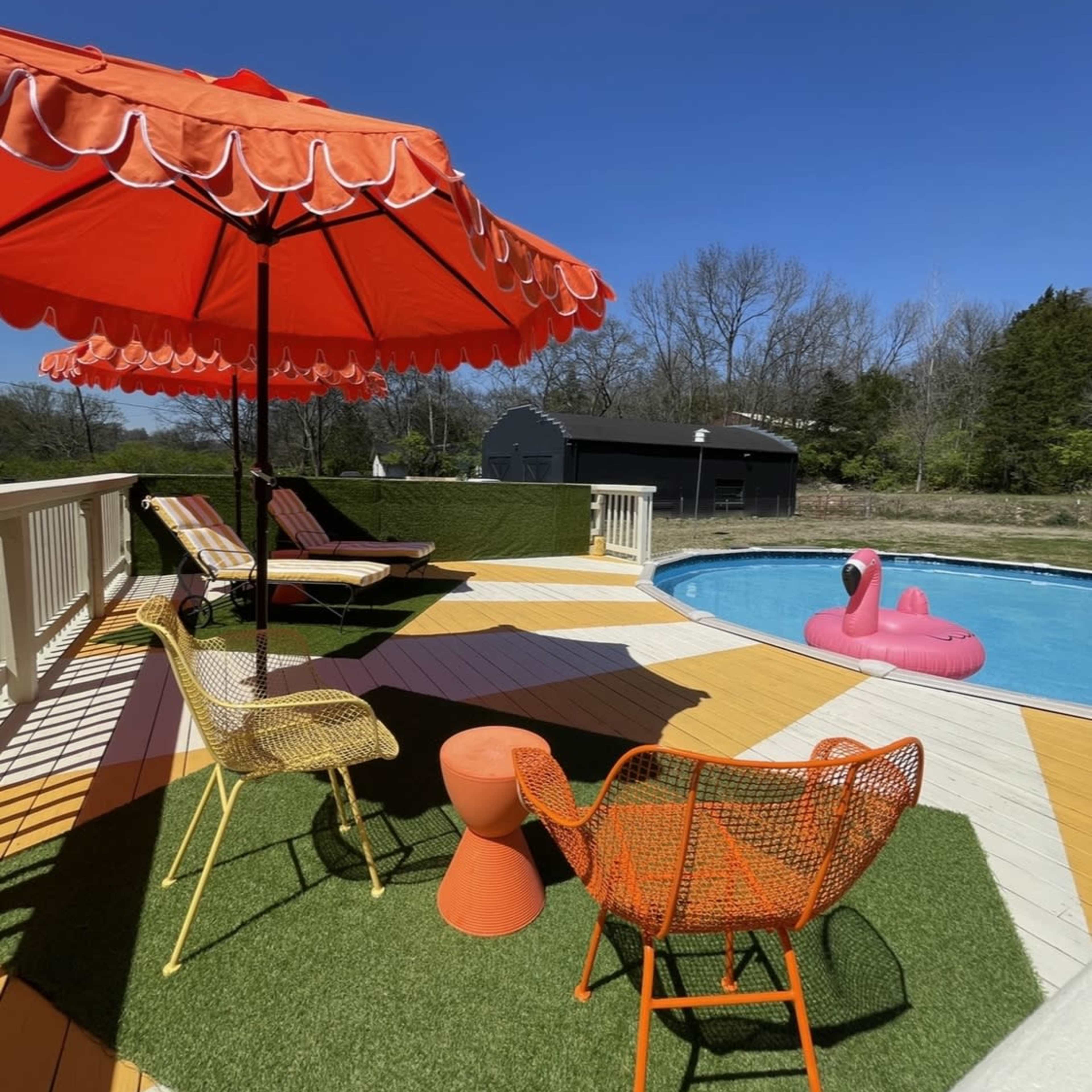 A colorful poolside scene features orange umbrellas, lounge chairs, and a pink flamingo float beside a blue swimming pool.