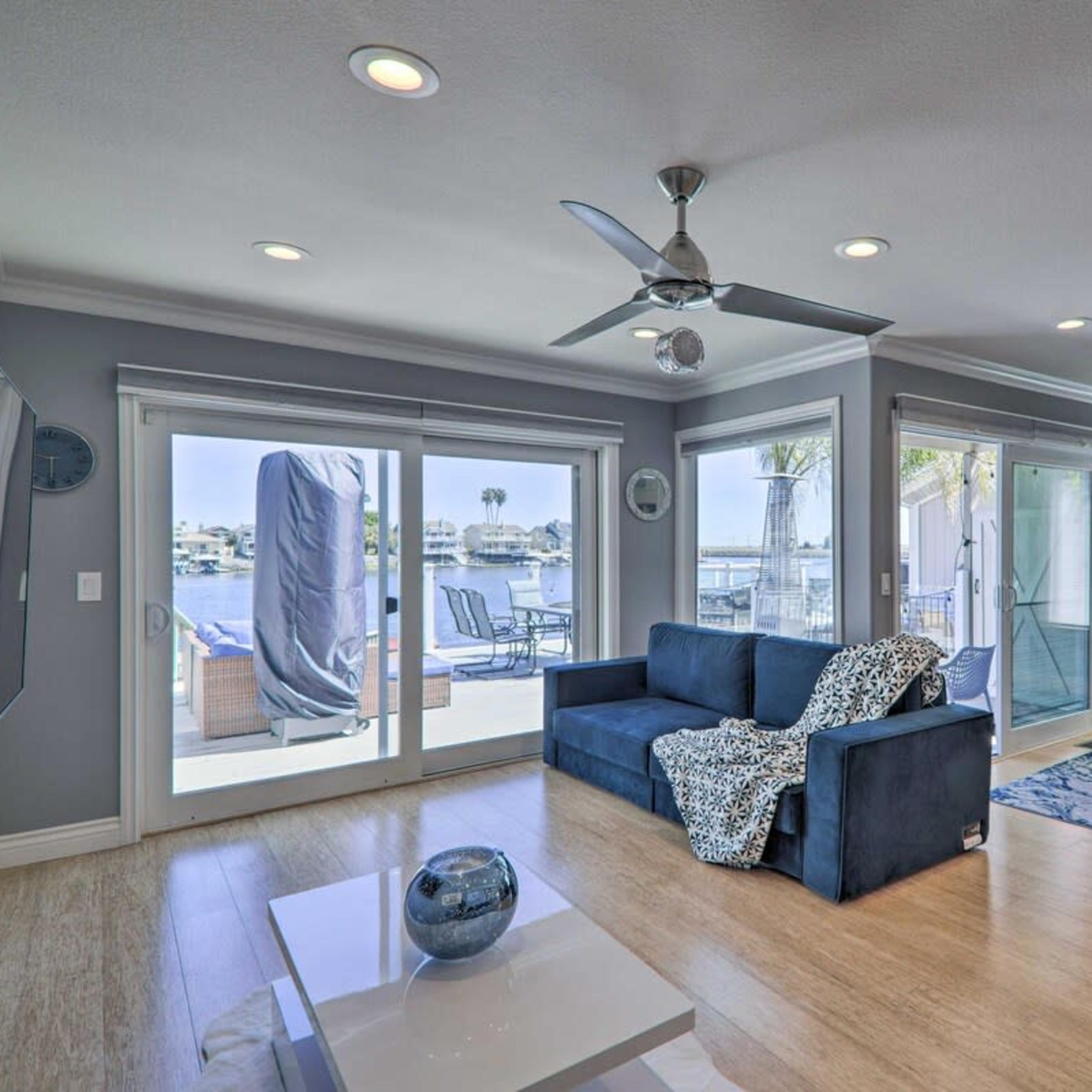 A living room with a sofa, dining area, and large windows that provide a view of a patio overlooking the water.