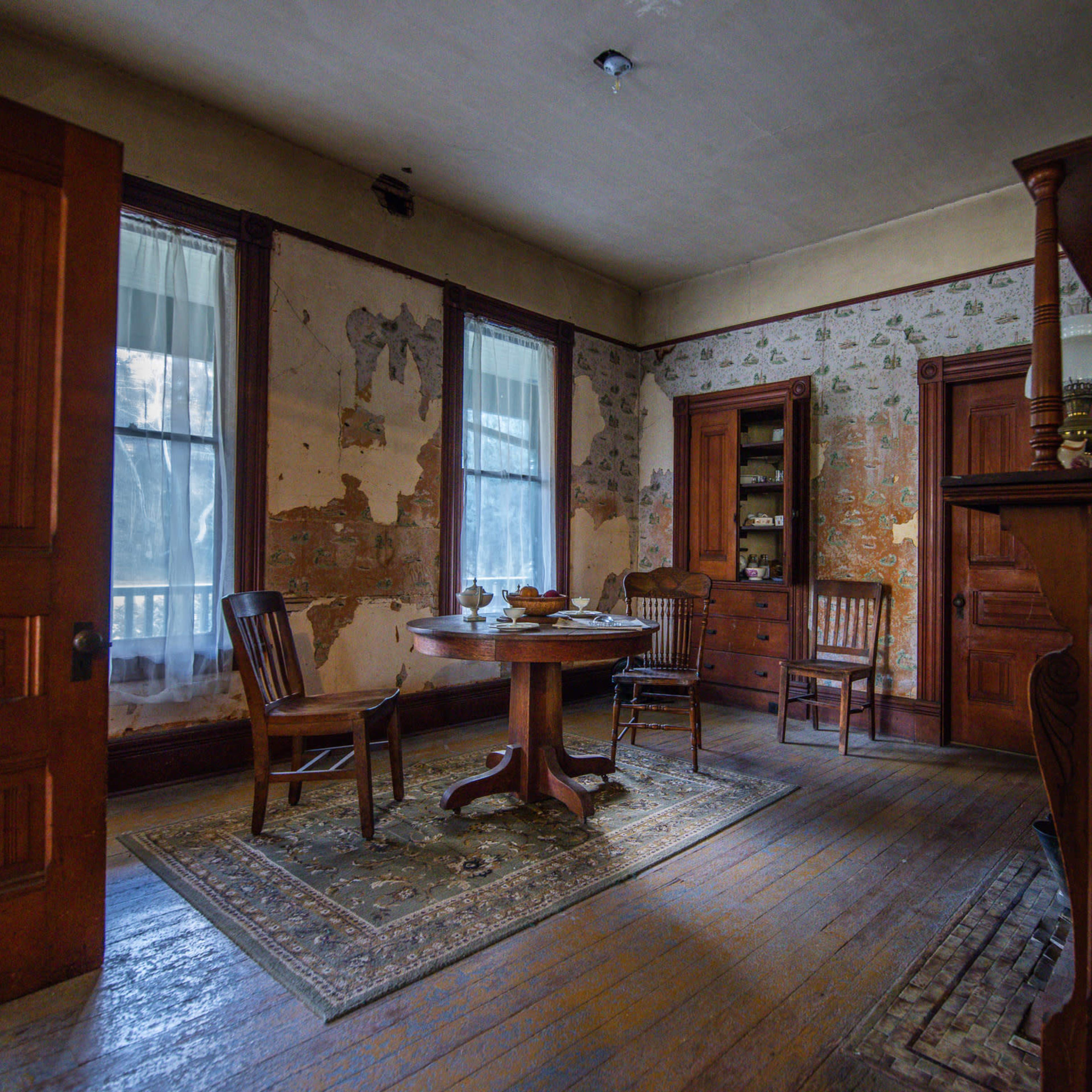 A vintage interior room with a round wooden table, four chairs, and peeling wallpaper.