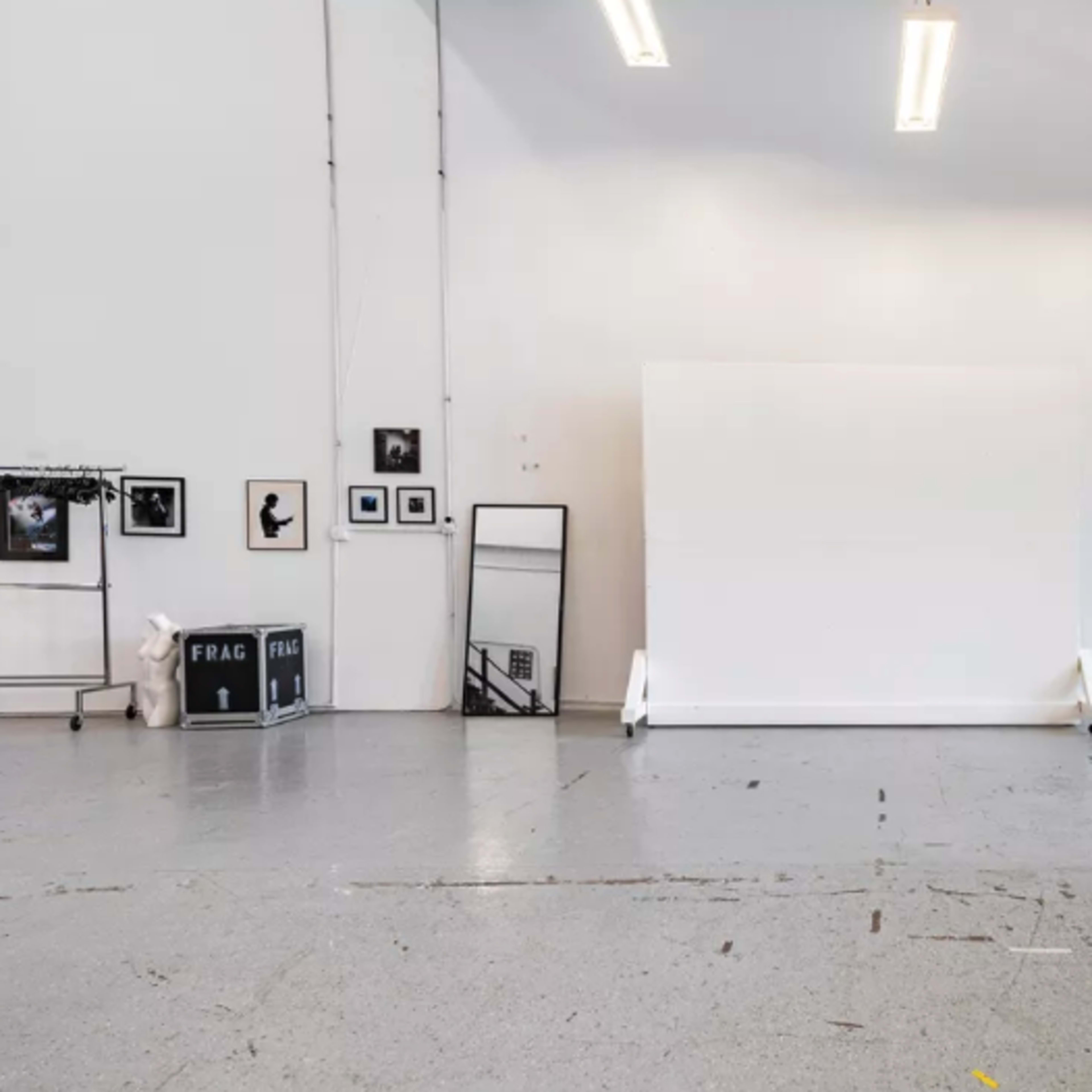A spacious, minimalist studio with a large white backdrop, framed photographs on the walls, and a window letting in natural light.