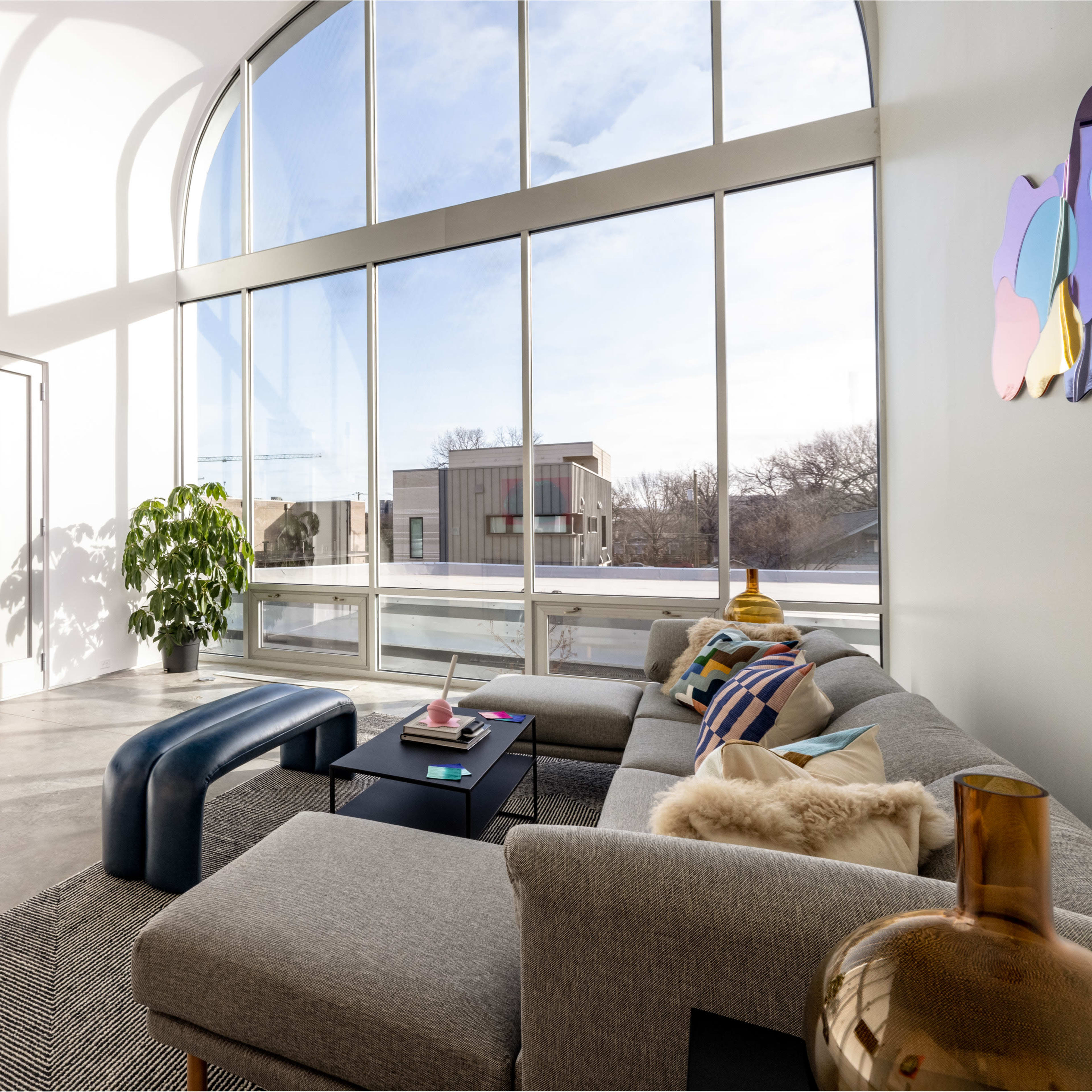 A bright living room features large windows, modern furniture, and a green plant near a gray sofa.