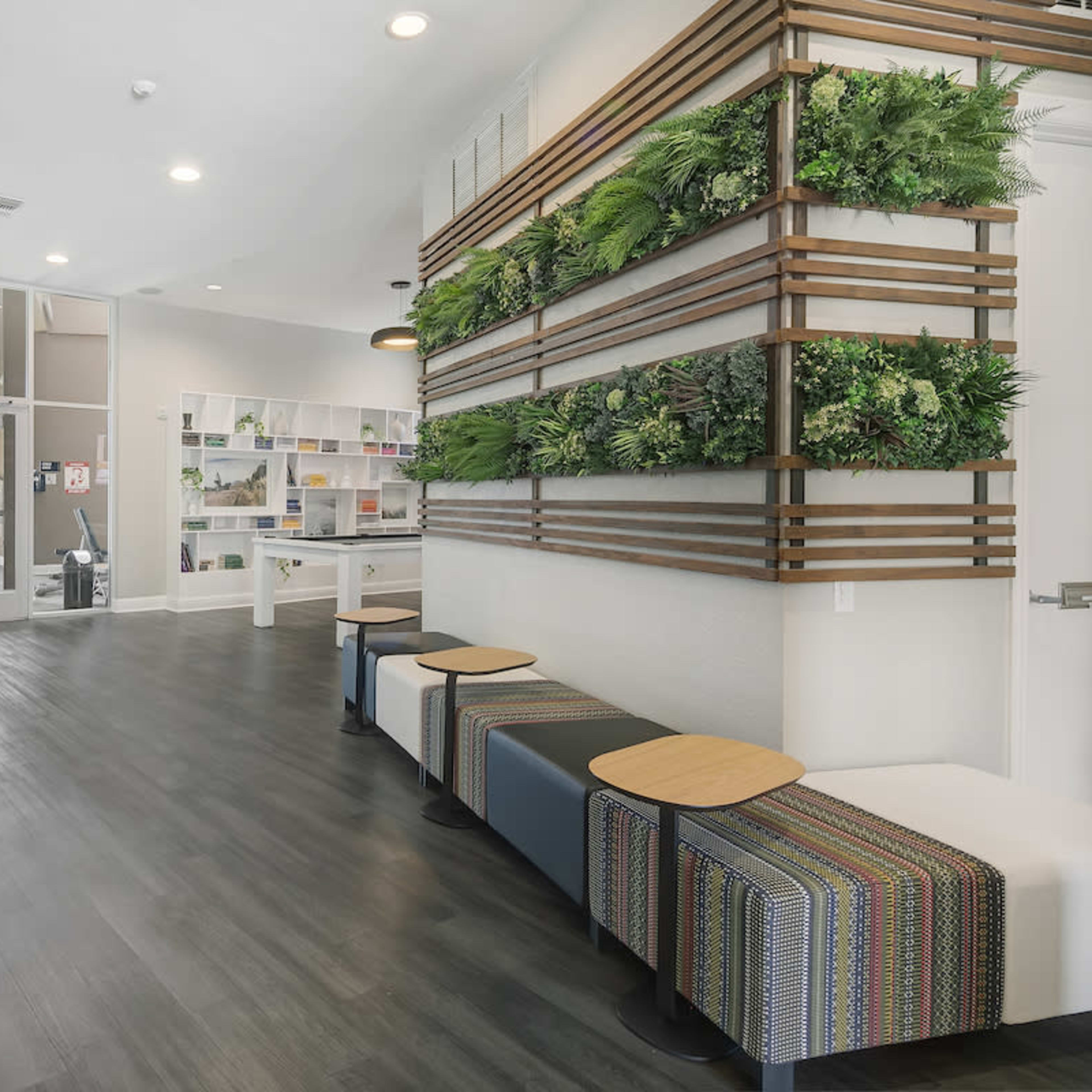 A modern interior space featuring a reception area with green wall decor, benches, and seating alongside a large glass entryway.