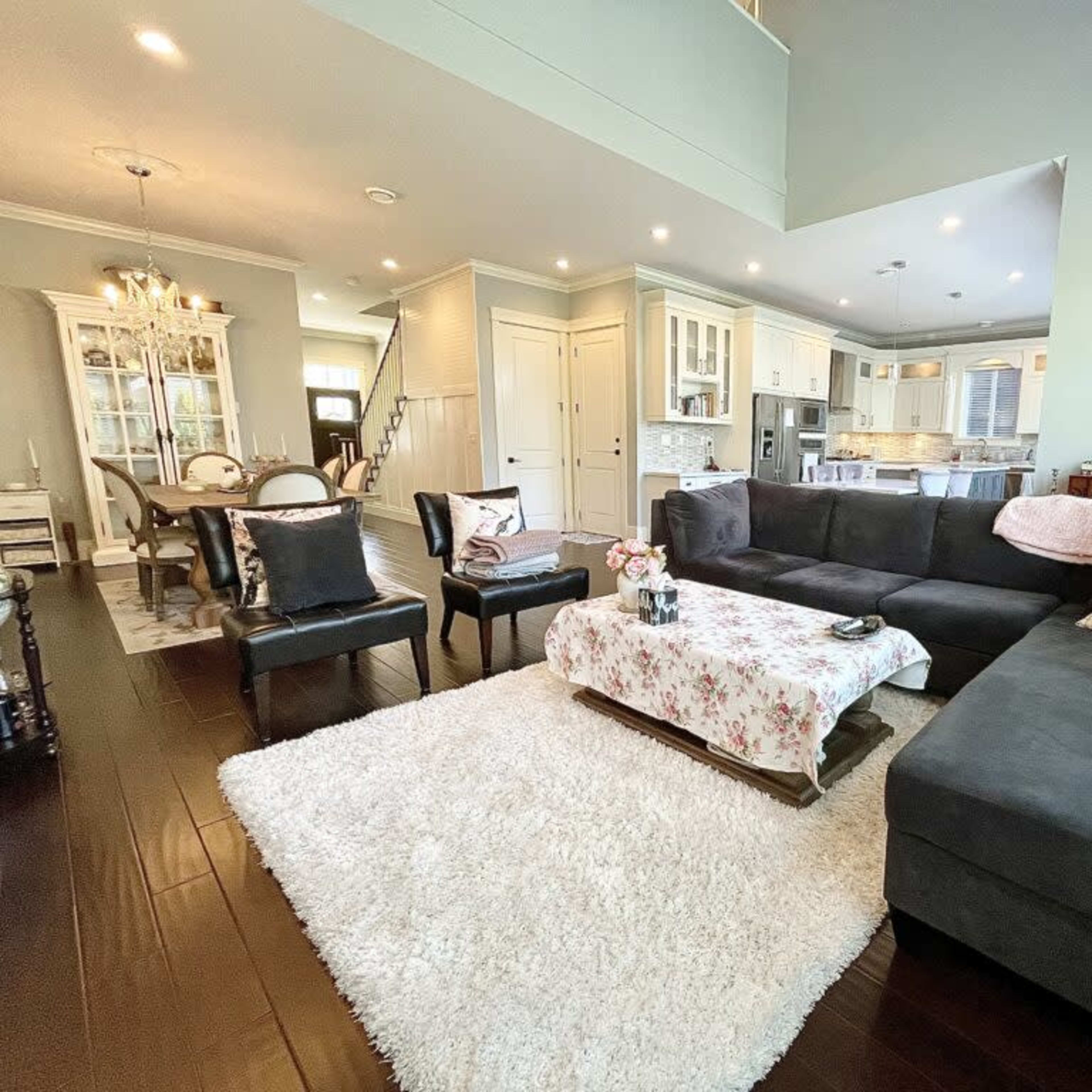 A modern living room with a dark sectional sofa, a floral-patterned coffee table cover, and a dining area visible in the background.