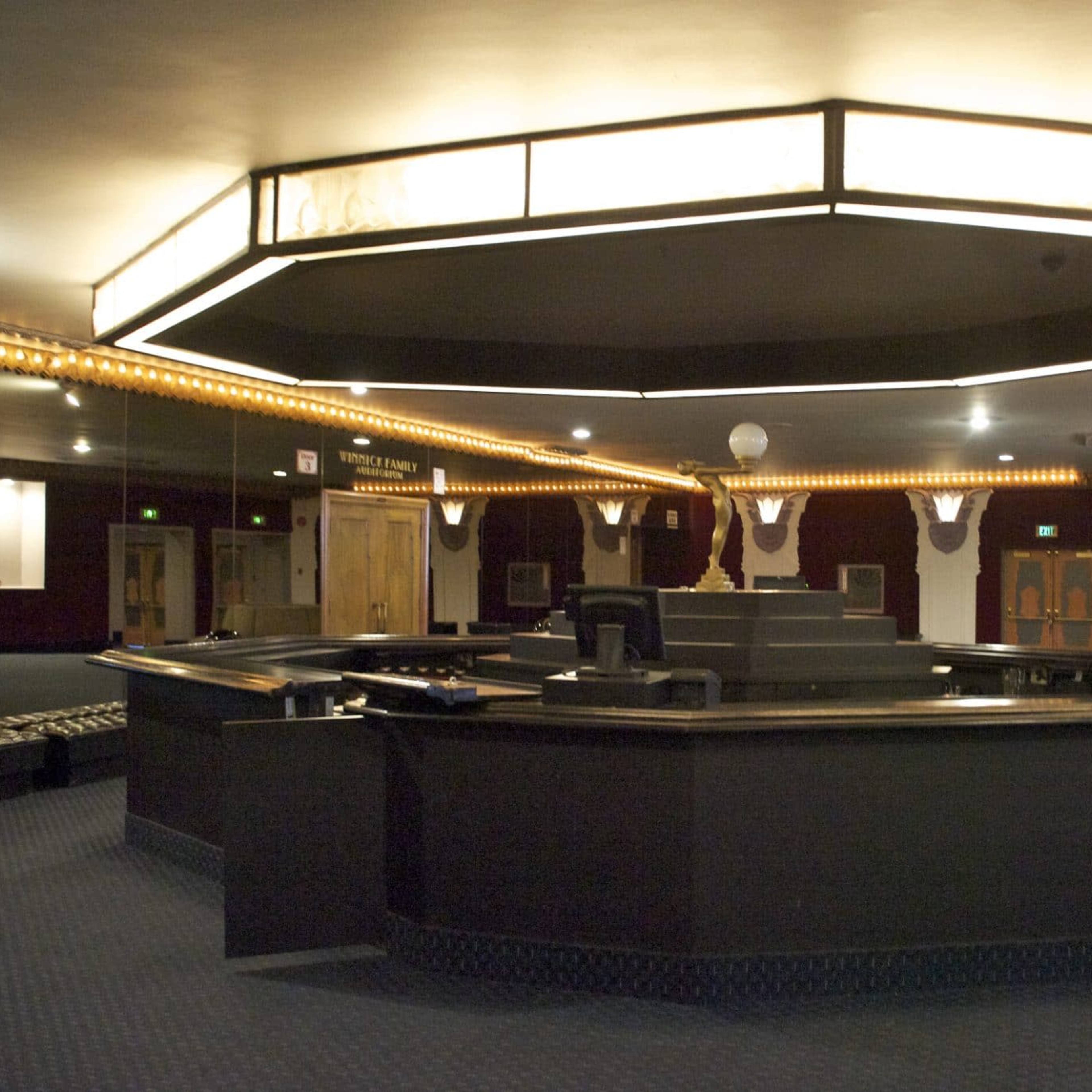 A spacious, dimly lit lobby with a large, modern reception desk and decorative lighting.