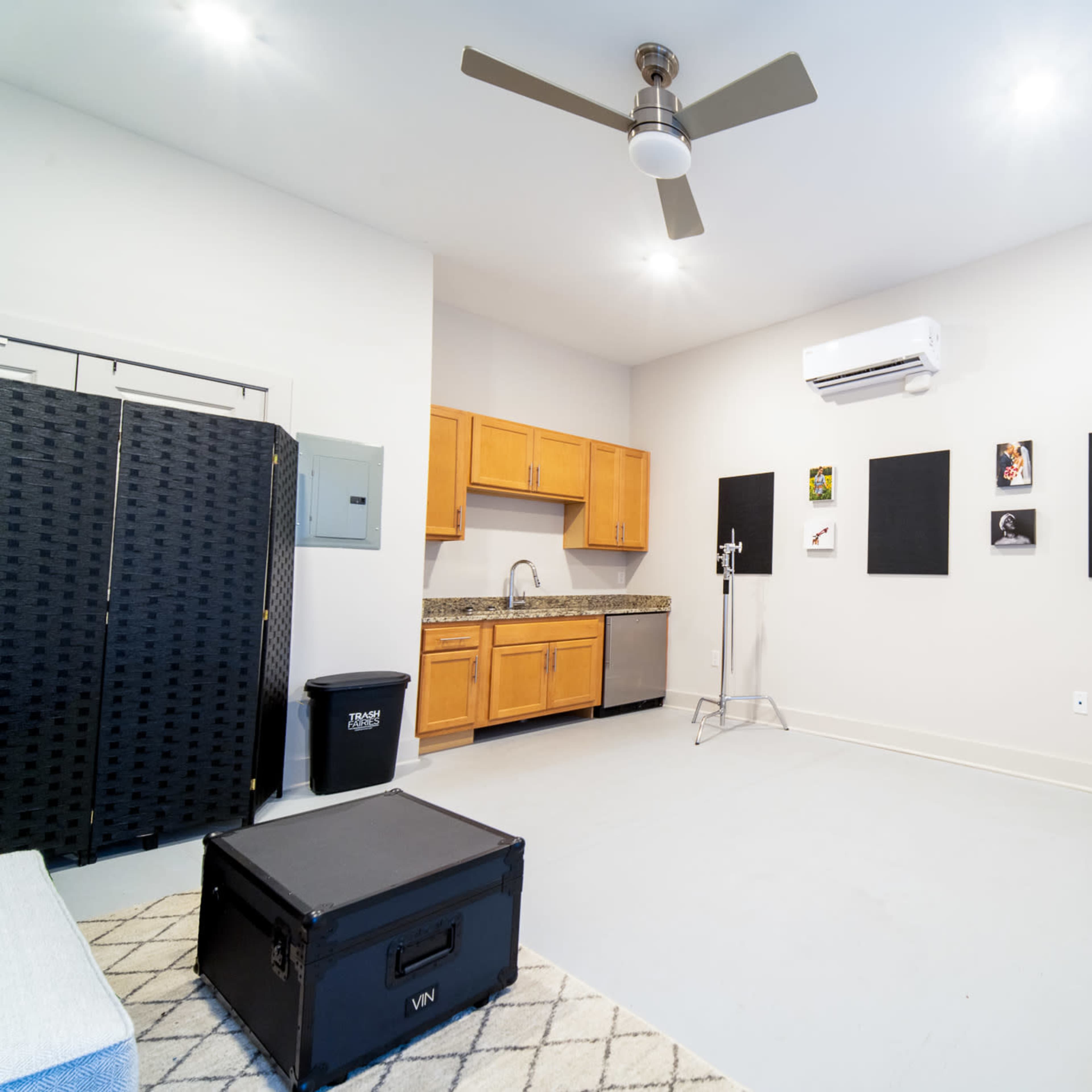 The room features a kitchenette with wooden cabinets, a black folding screen, and several framed artworks on the walls.