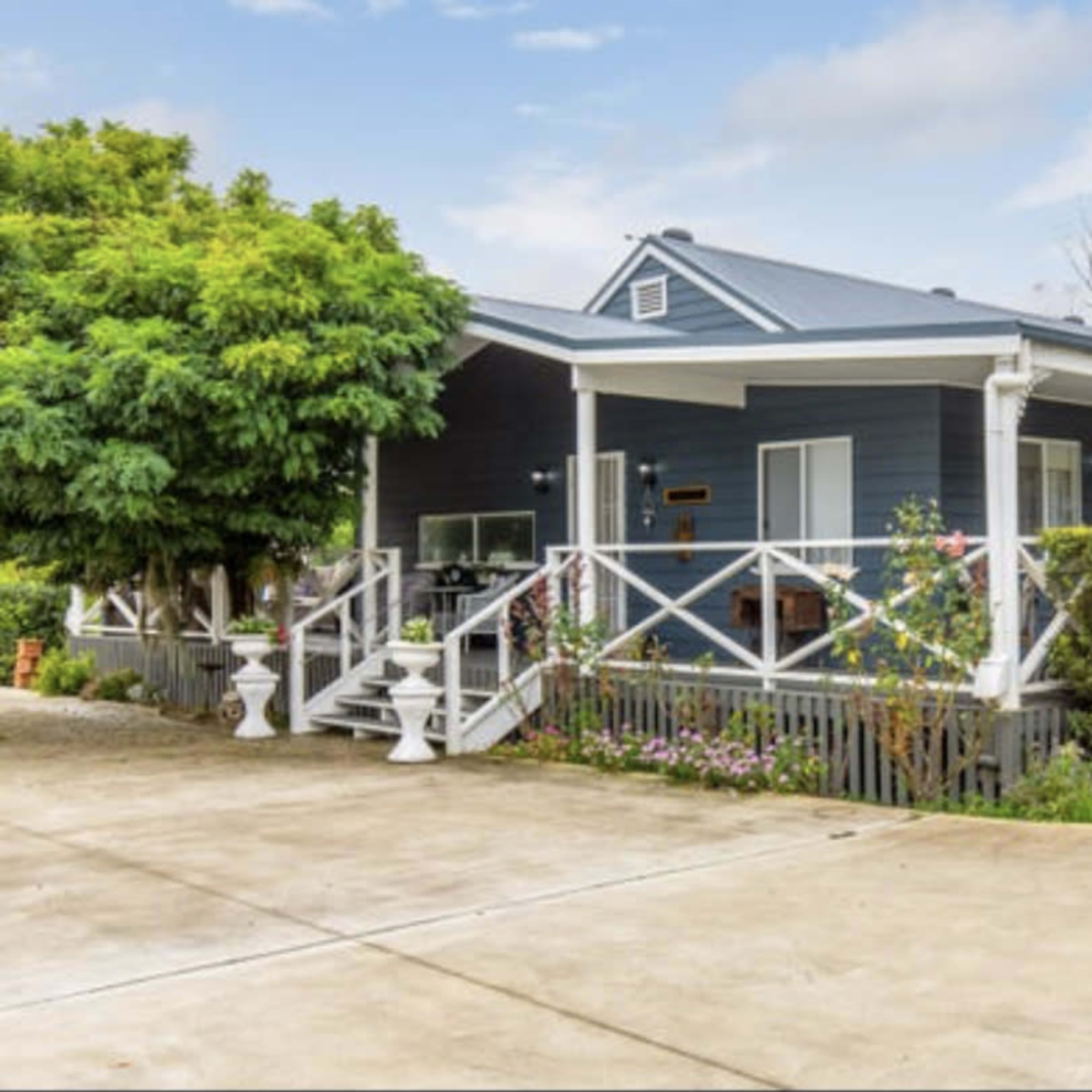 A blue house with a covered porch, surrounded by greenery and featuring a wide driveway.