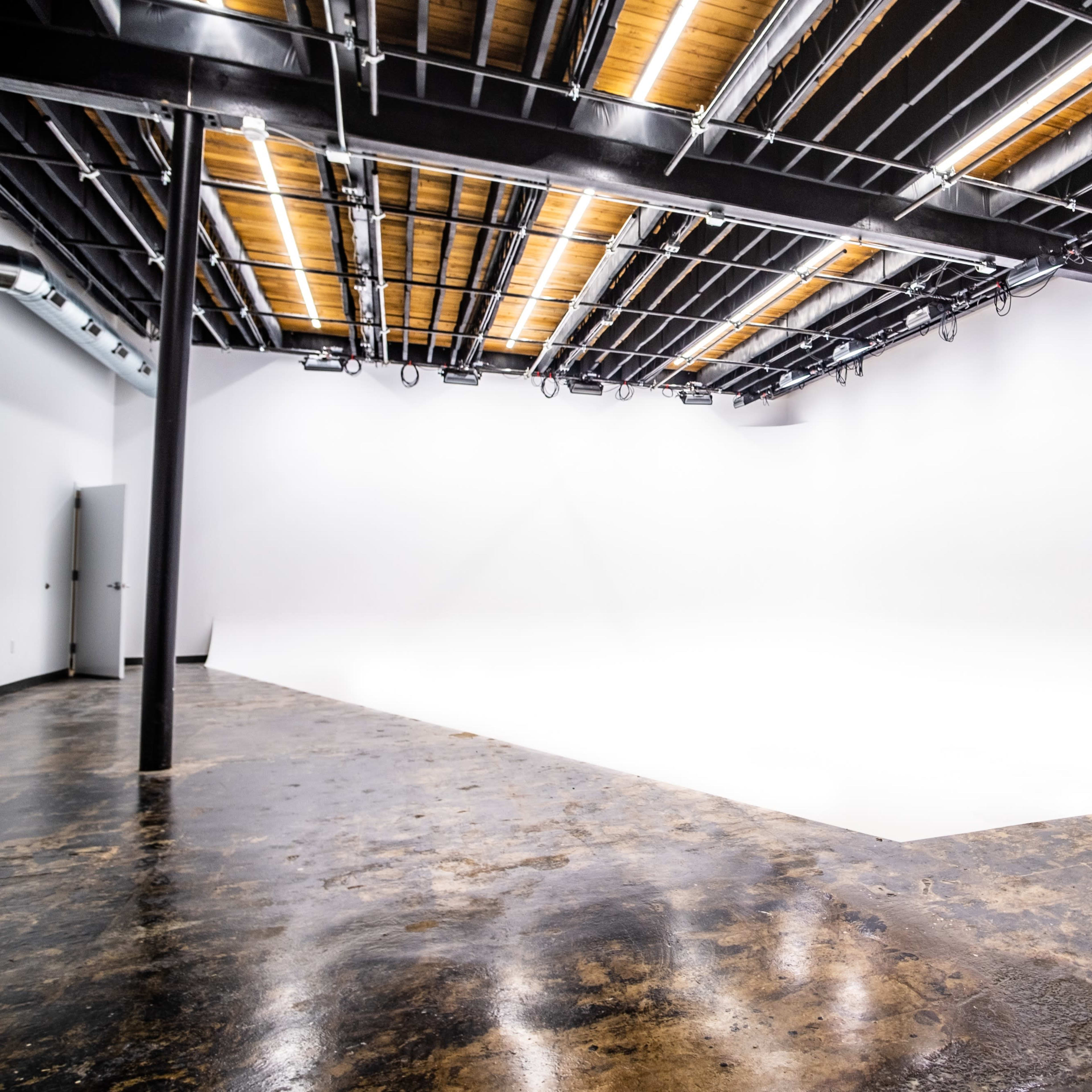 A spacious, empty photography studio with a seamless white backdrop and a polished concrete floor.