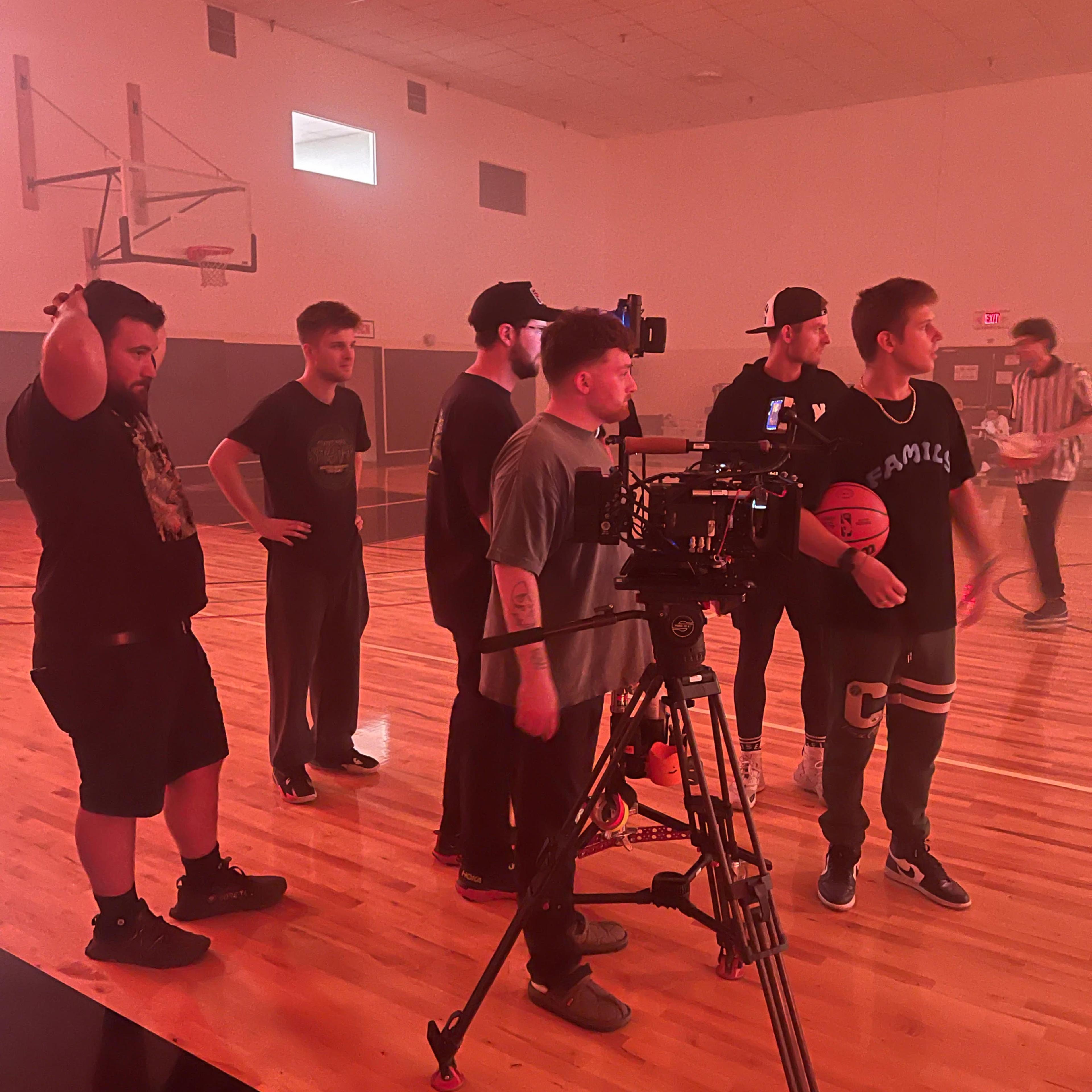 A group of people stands near a professional camera setup on a basketball court.