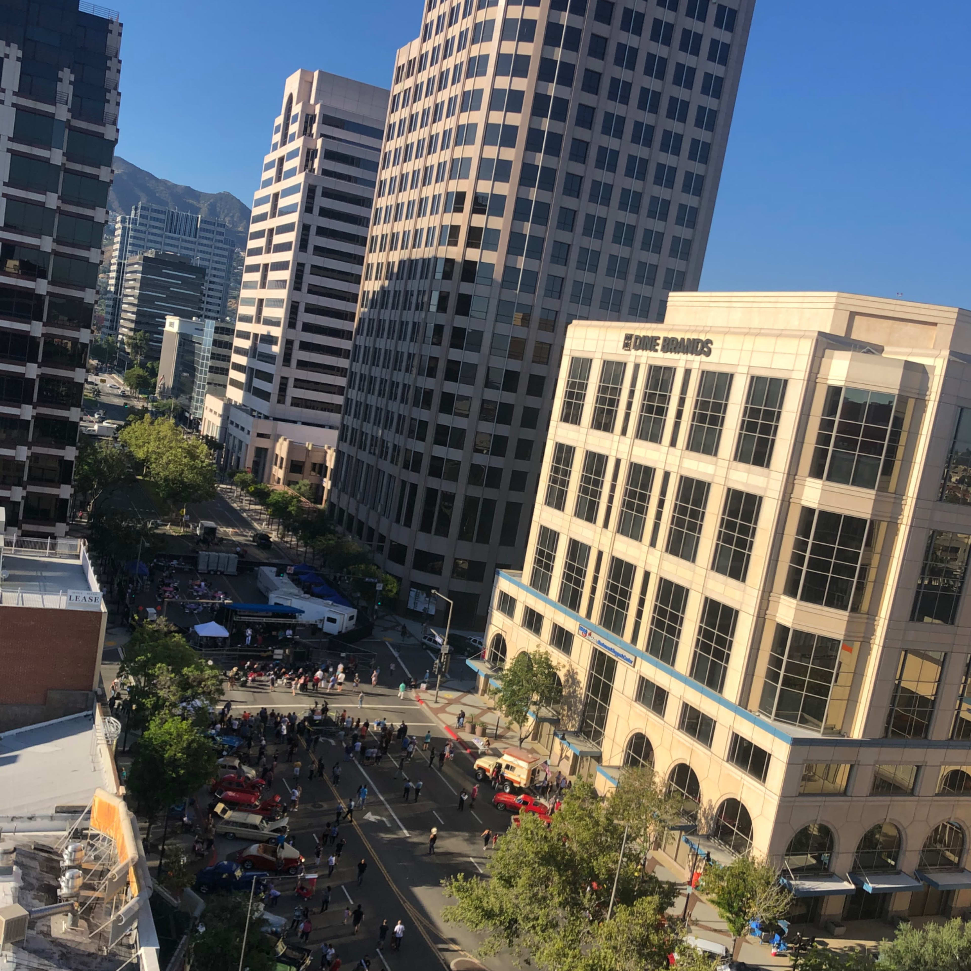 A bustling city street with tall buildings, trees lining the sidewalk, and a crowd of people gathered below.