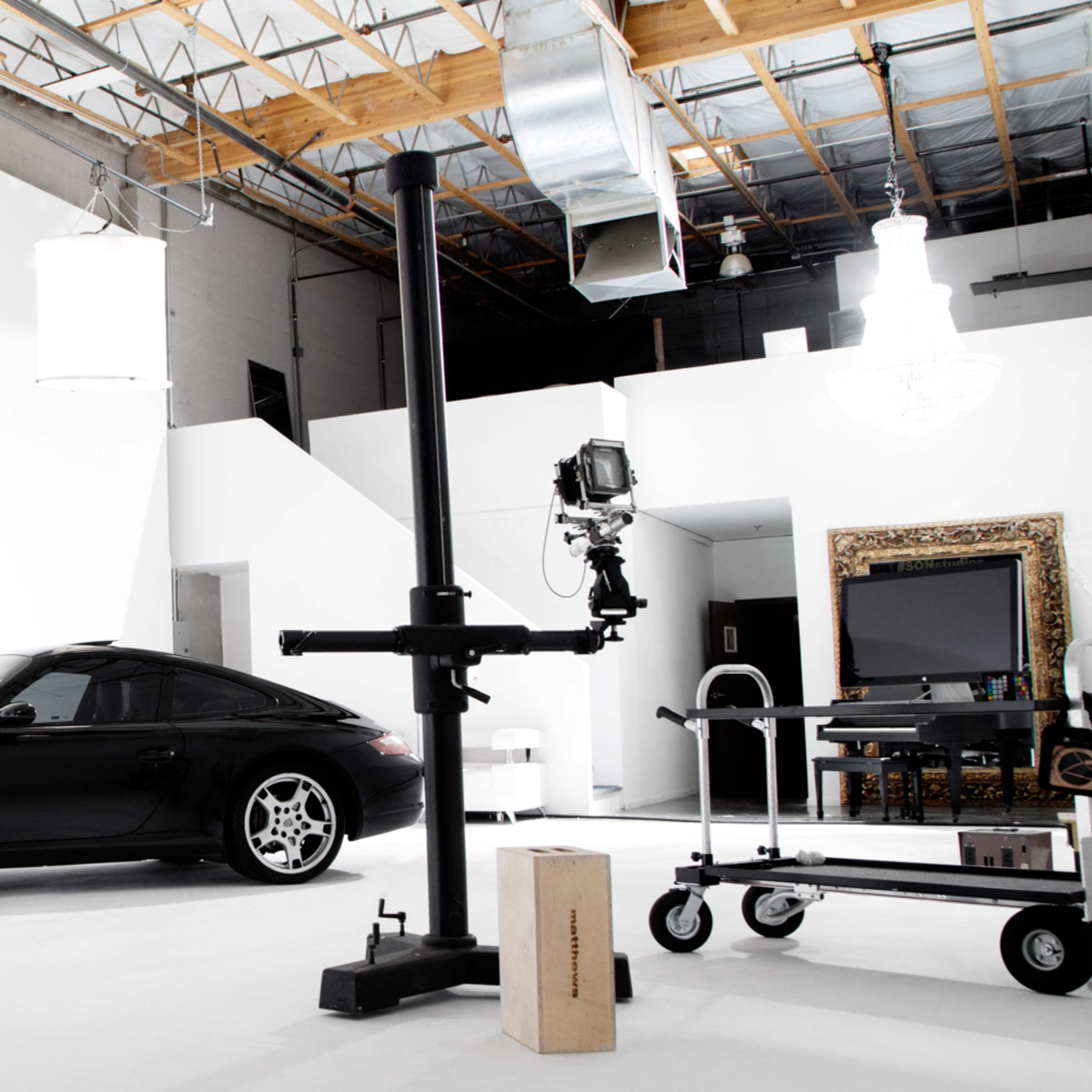 A classic black Ford Mustang convertible is parked in a spacious, well-lit photography studio with a spiral staircase in the background.