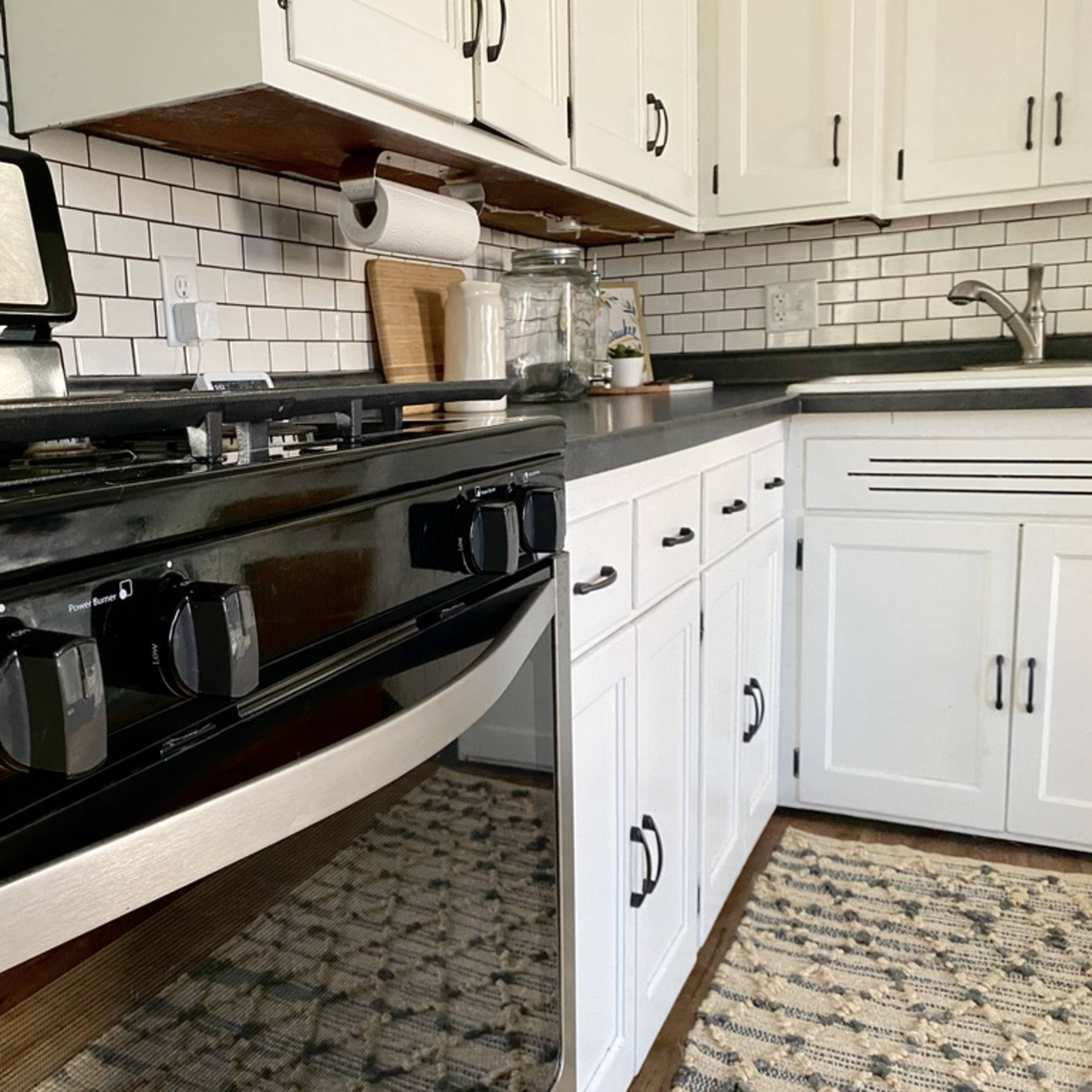 A modern kitchen featuring a black gas stove, white cabinetry, and a patterned rug on the floor.