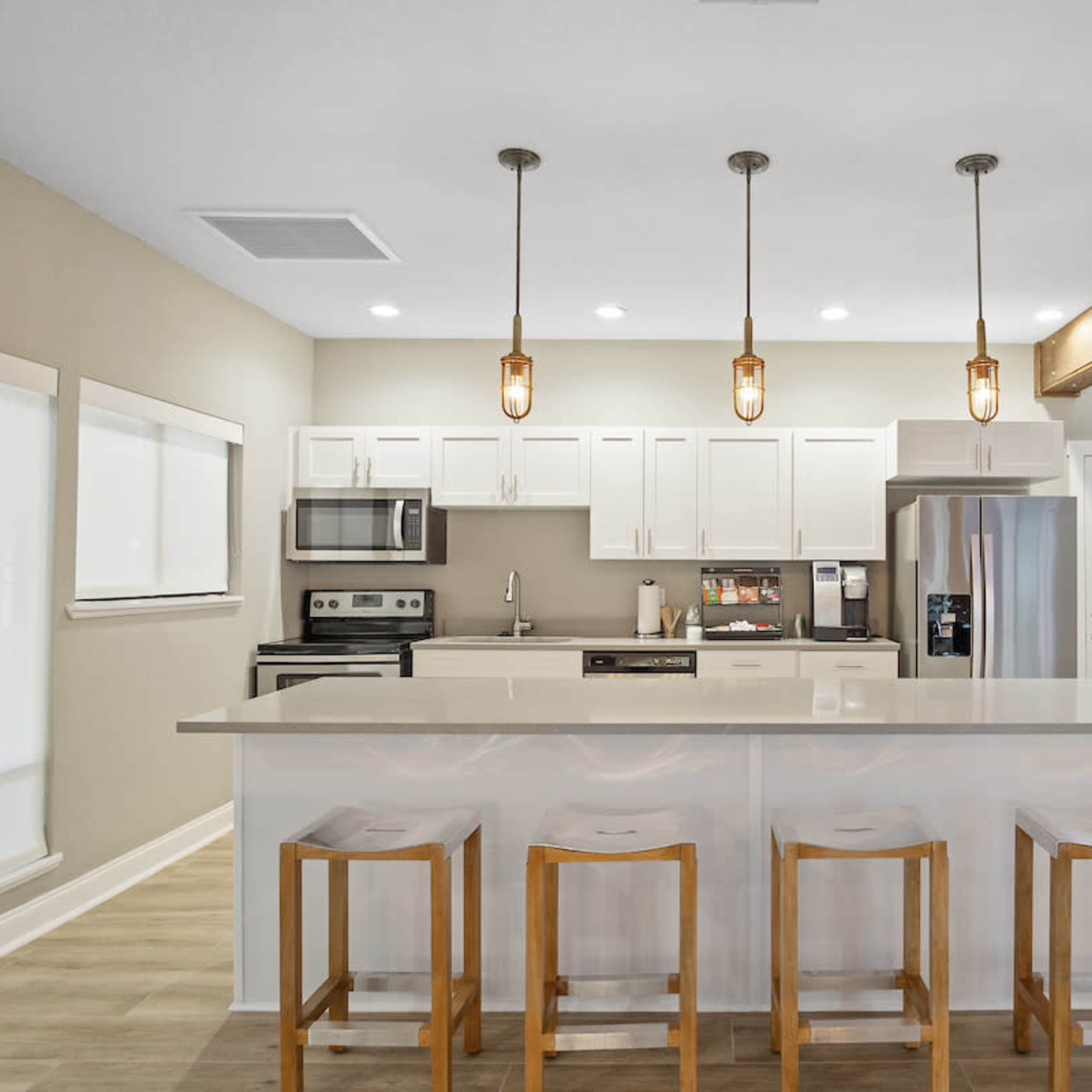 A modern kitchen features white cabinetry, stainless steel appliances, and a central island with four wooden barstools.
