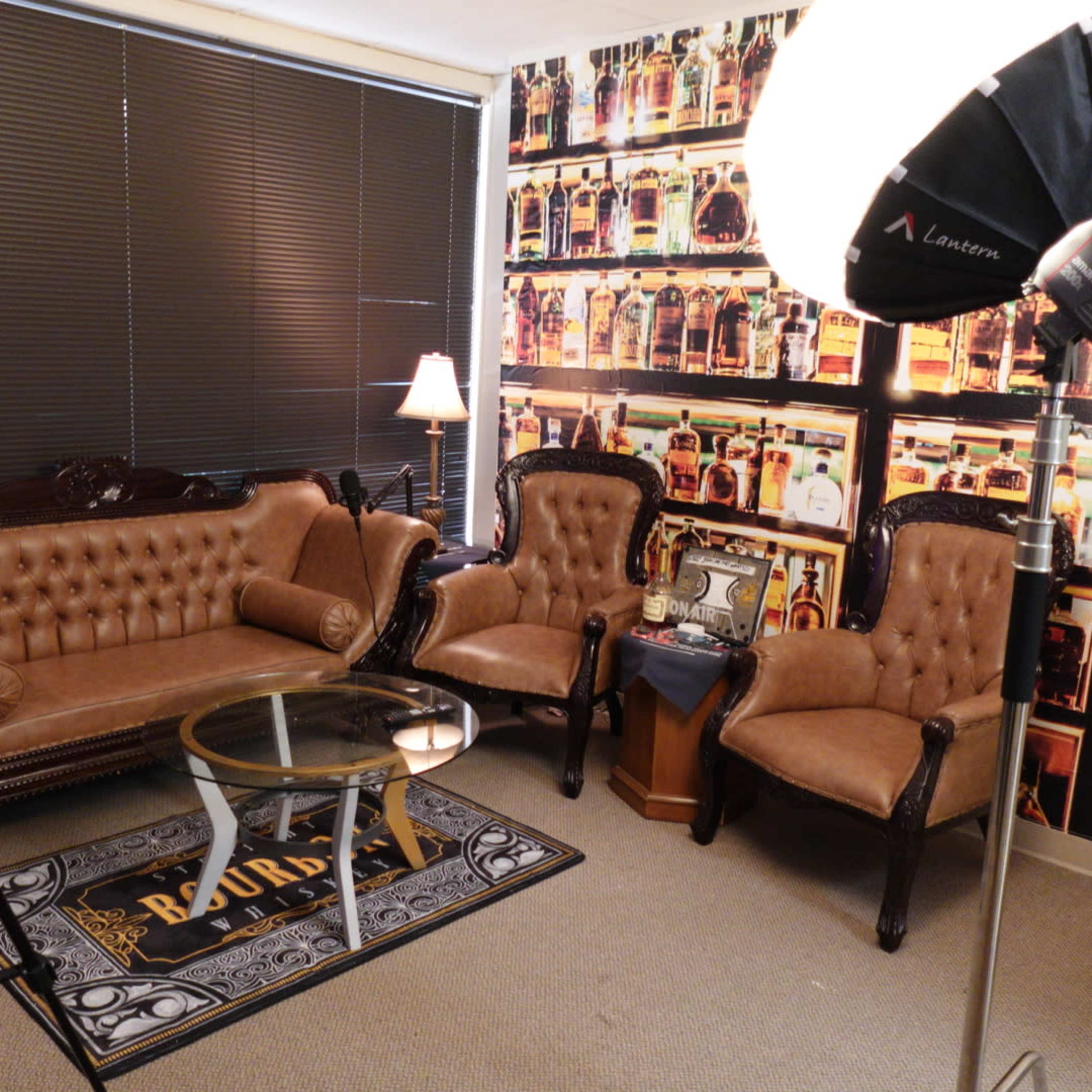 A small room furnished with a brown leather sofa, two matching armchairs, a glass coffee table, and a backdrop of a wall covered in a patterned wallpaper featuring images of bottles.