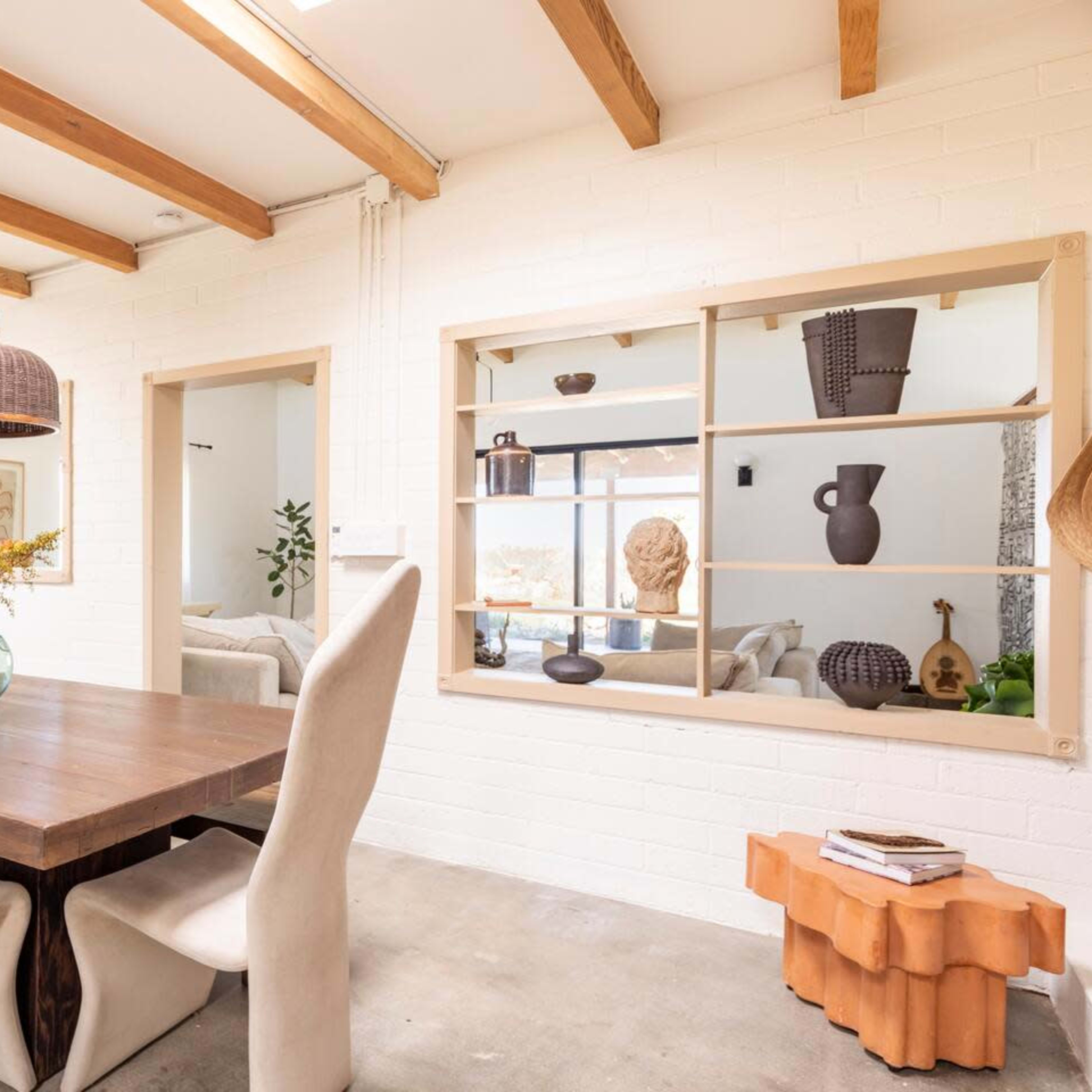 A spacious dining area features a wooden table surrounded by upholstered chairs, with large windows and exposed beams overhead.