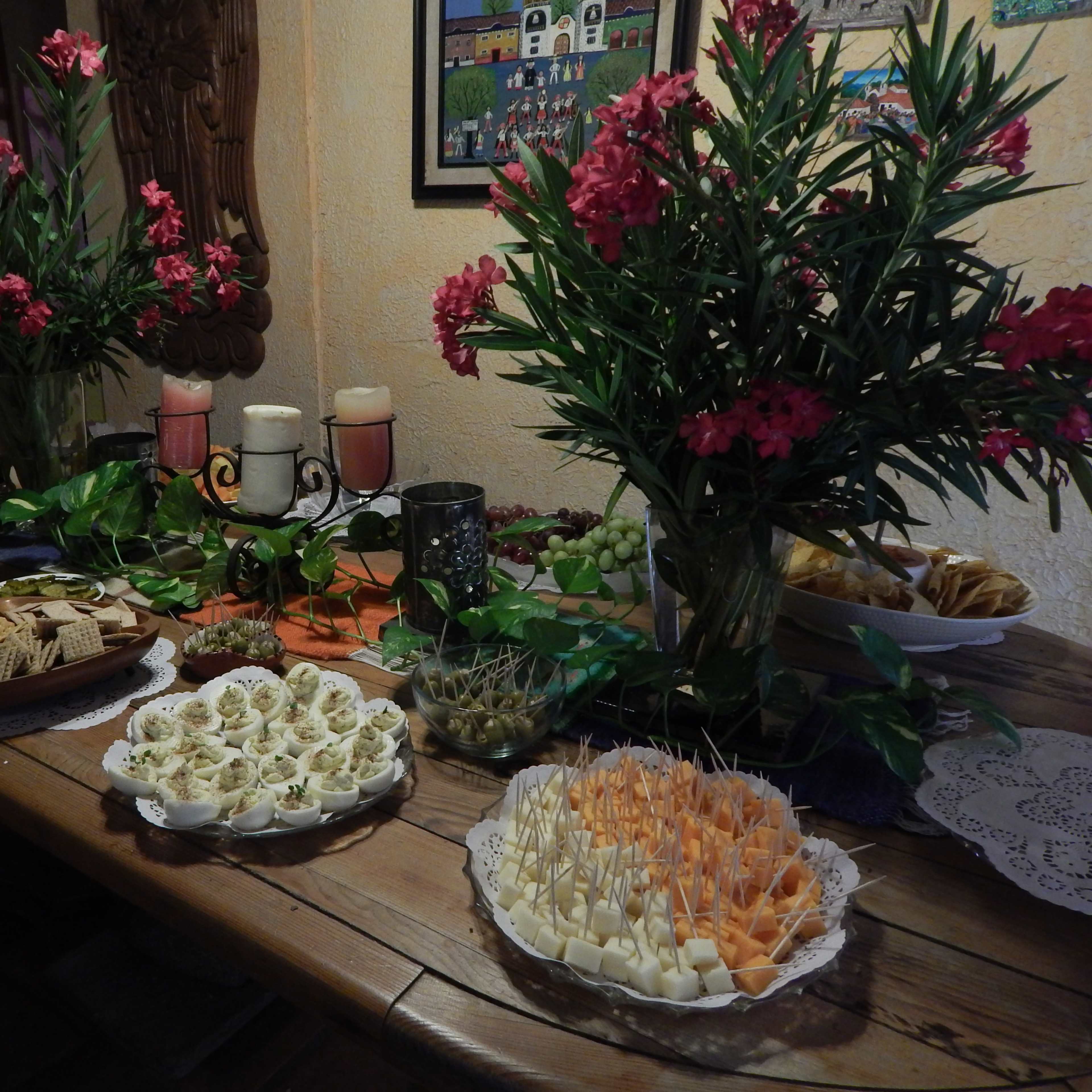 A wooden table set with various platters of food, including meats, cheeses, crackers, and decorative flowers in vases.