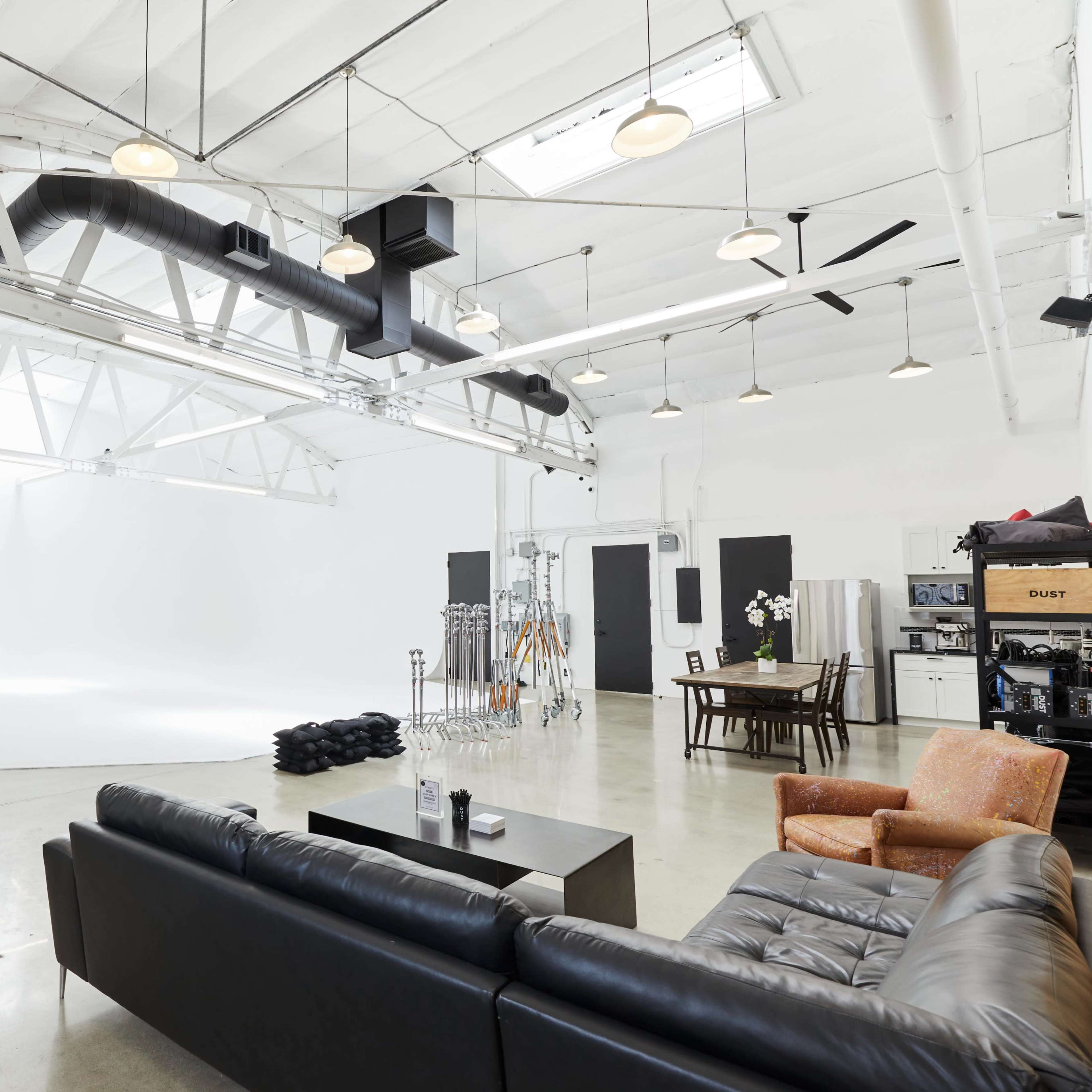 A spacious photography studio with a white backdrop, seating area, and various lighting equipment positioned along the walls.