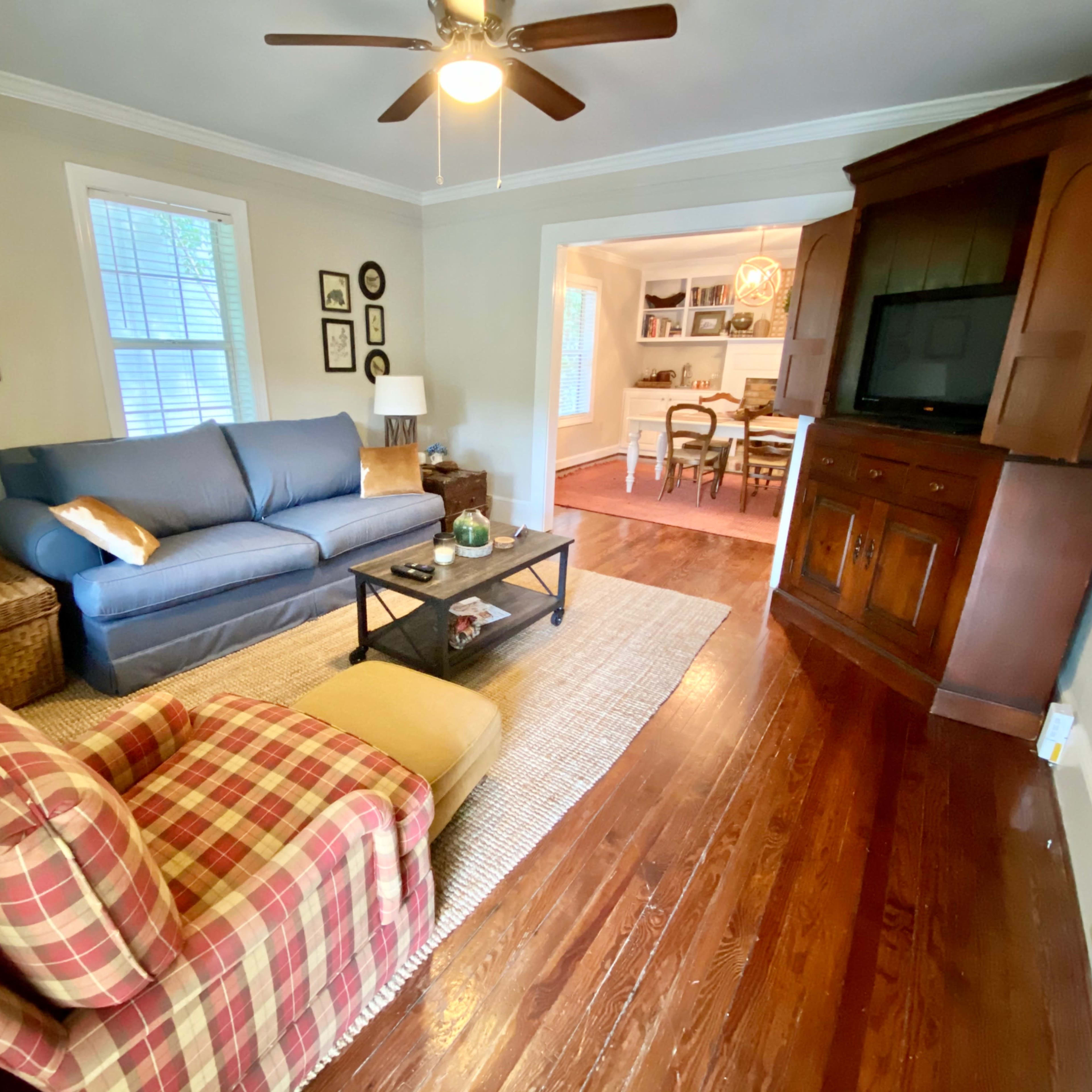 A living room with a blue sofa, a patterned chair, and a wooden TV cabinet, all situated on polished wooden floors.