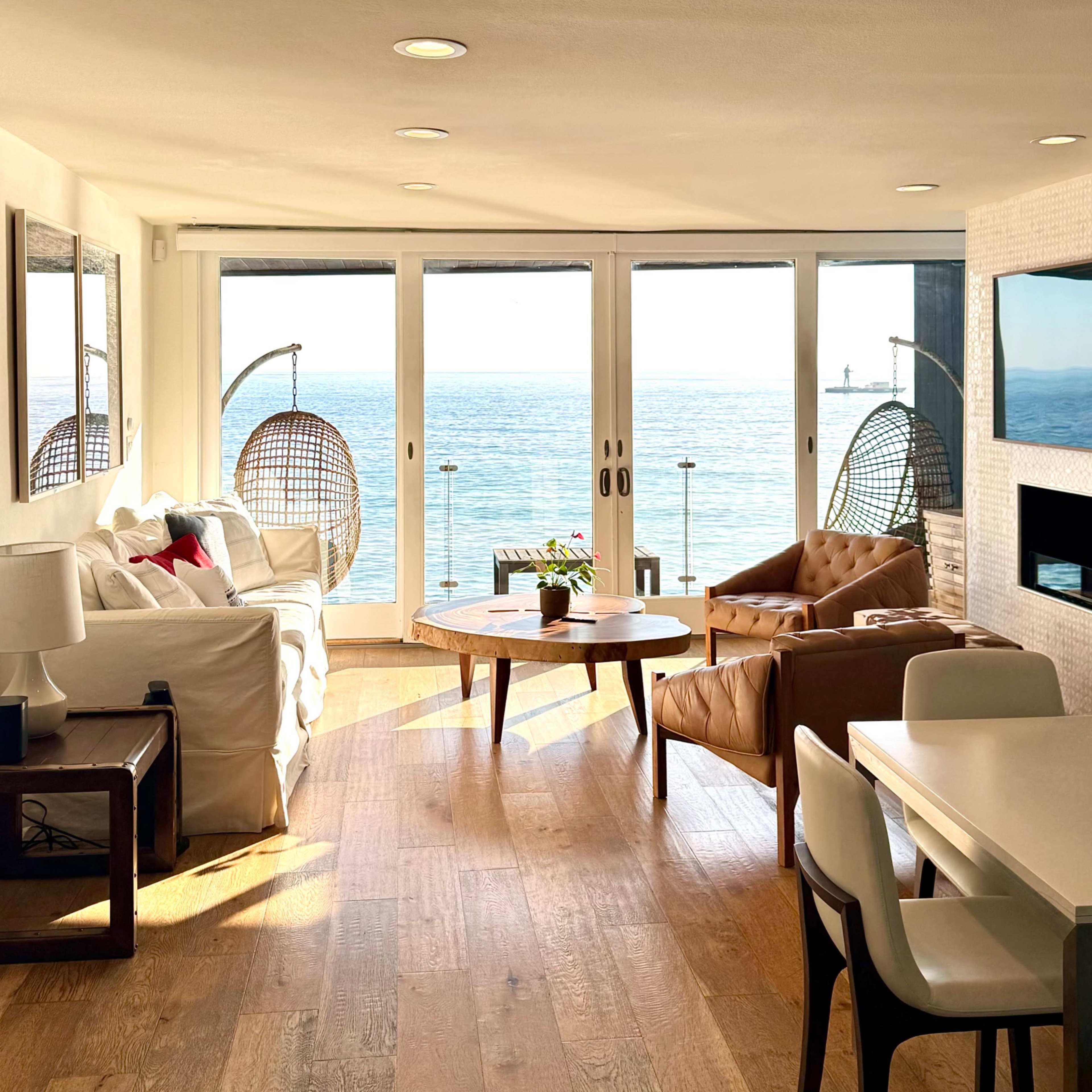 A modern living space features a cozy seating area, a dining table, and large glass doors offering a view of the ocean.
