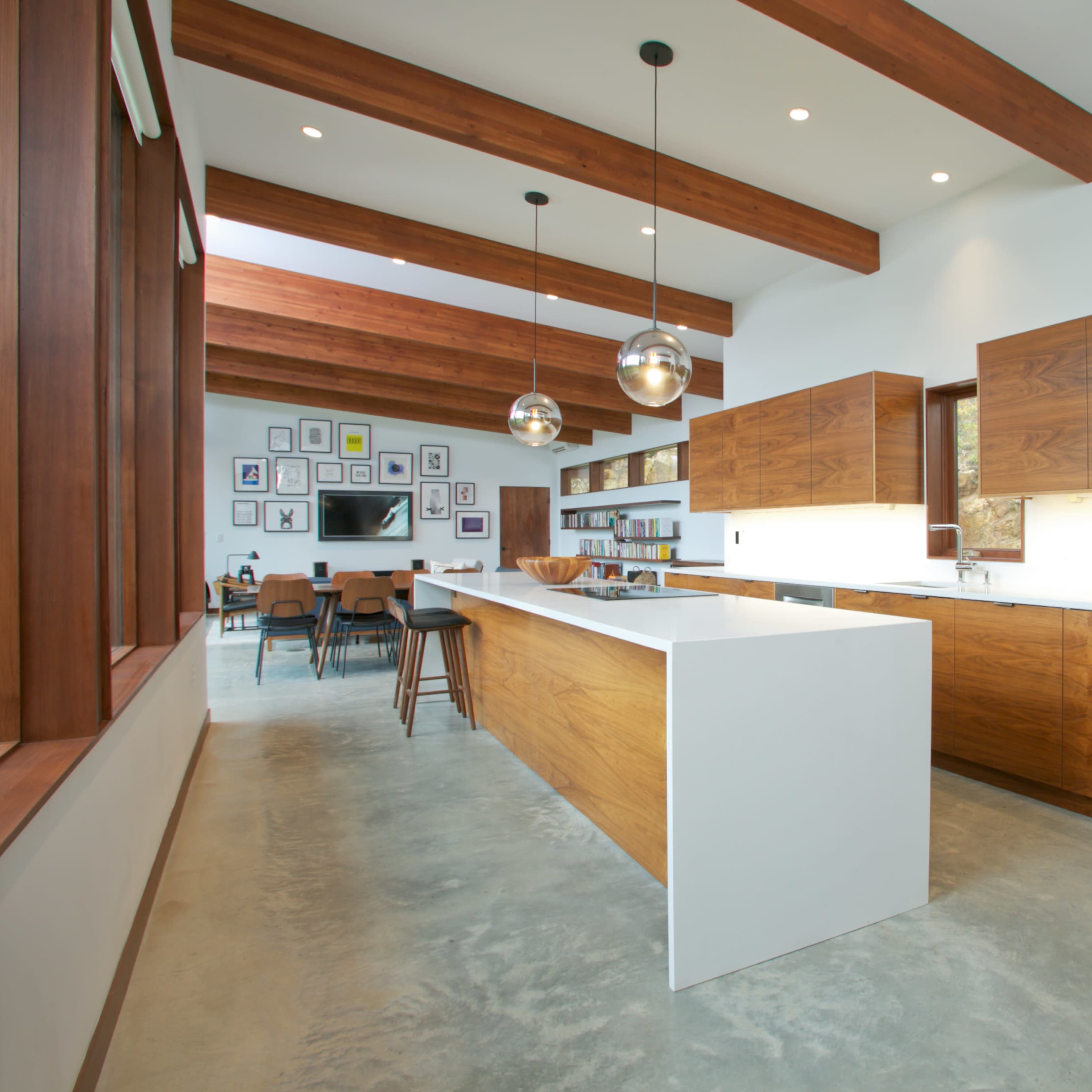 A modern kitchen with wooden cabinets, a large white island, and exposed wooden beams overhead.