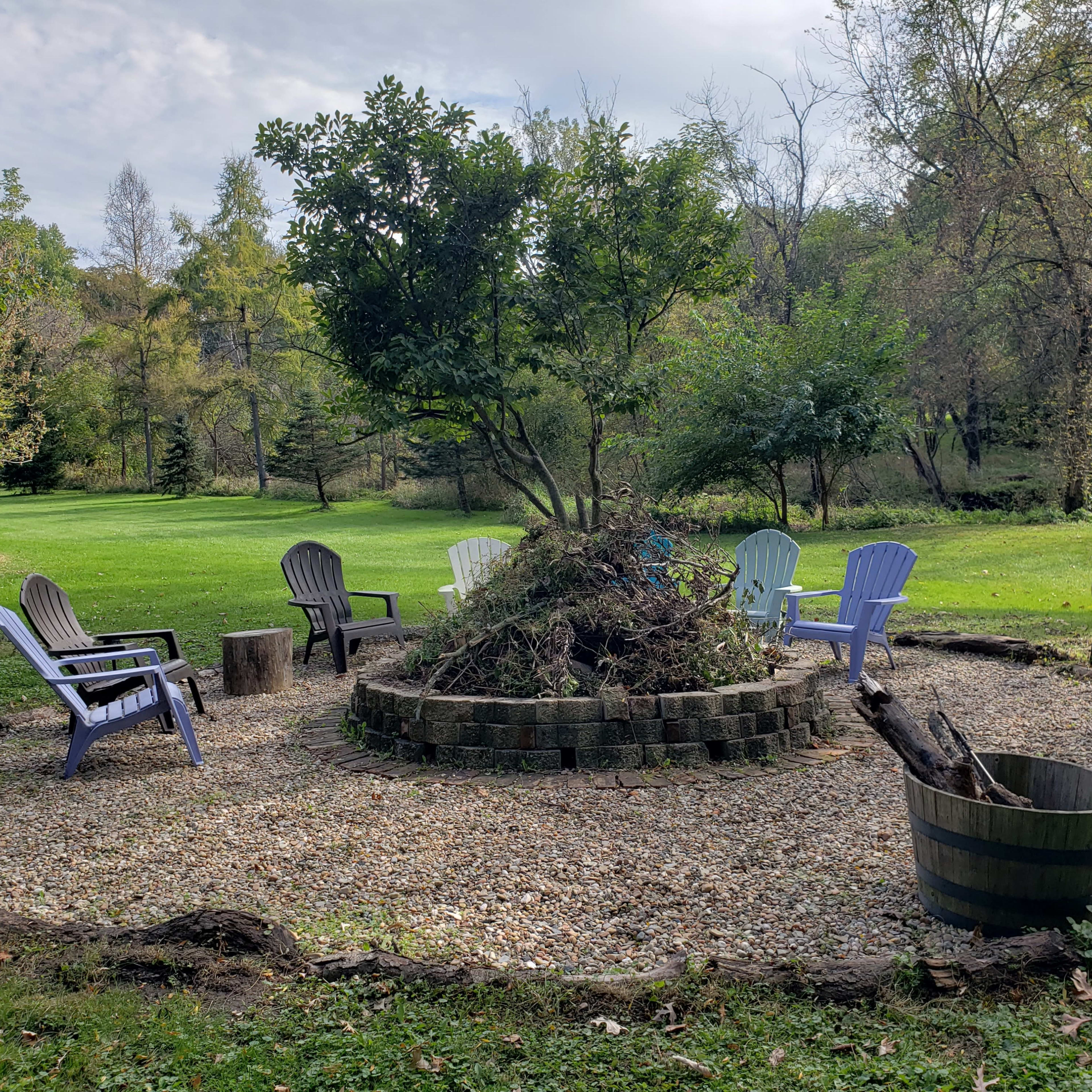 A circular seating area with multiple chairs surrounds a small pile of brush and debris in a grassy outdoor space.