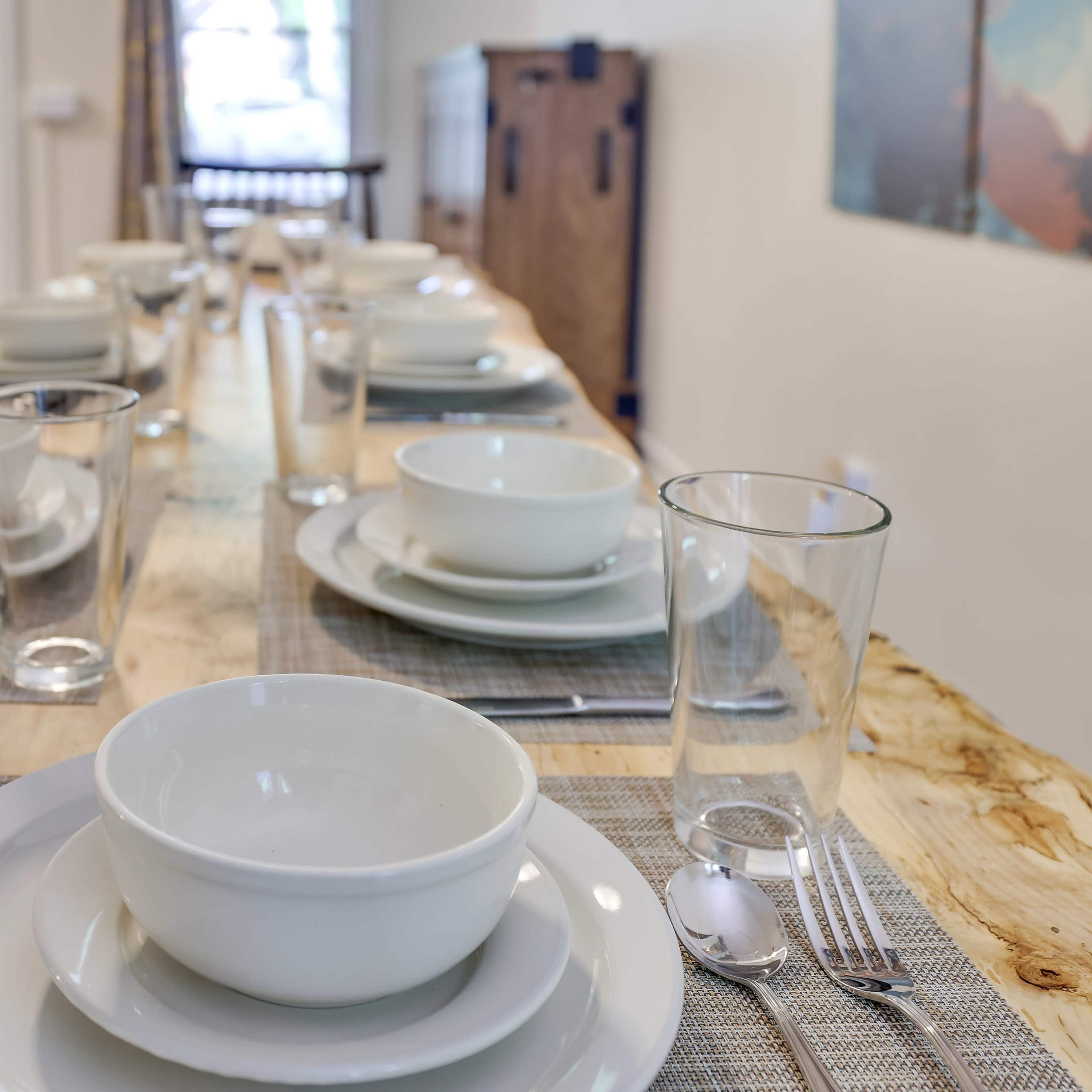 A long dining table is set with white dishes, glasses, and utensils, ready for a meal.