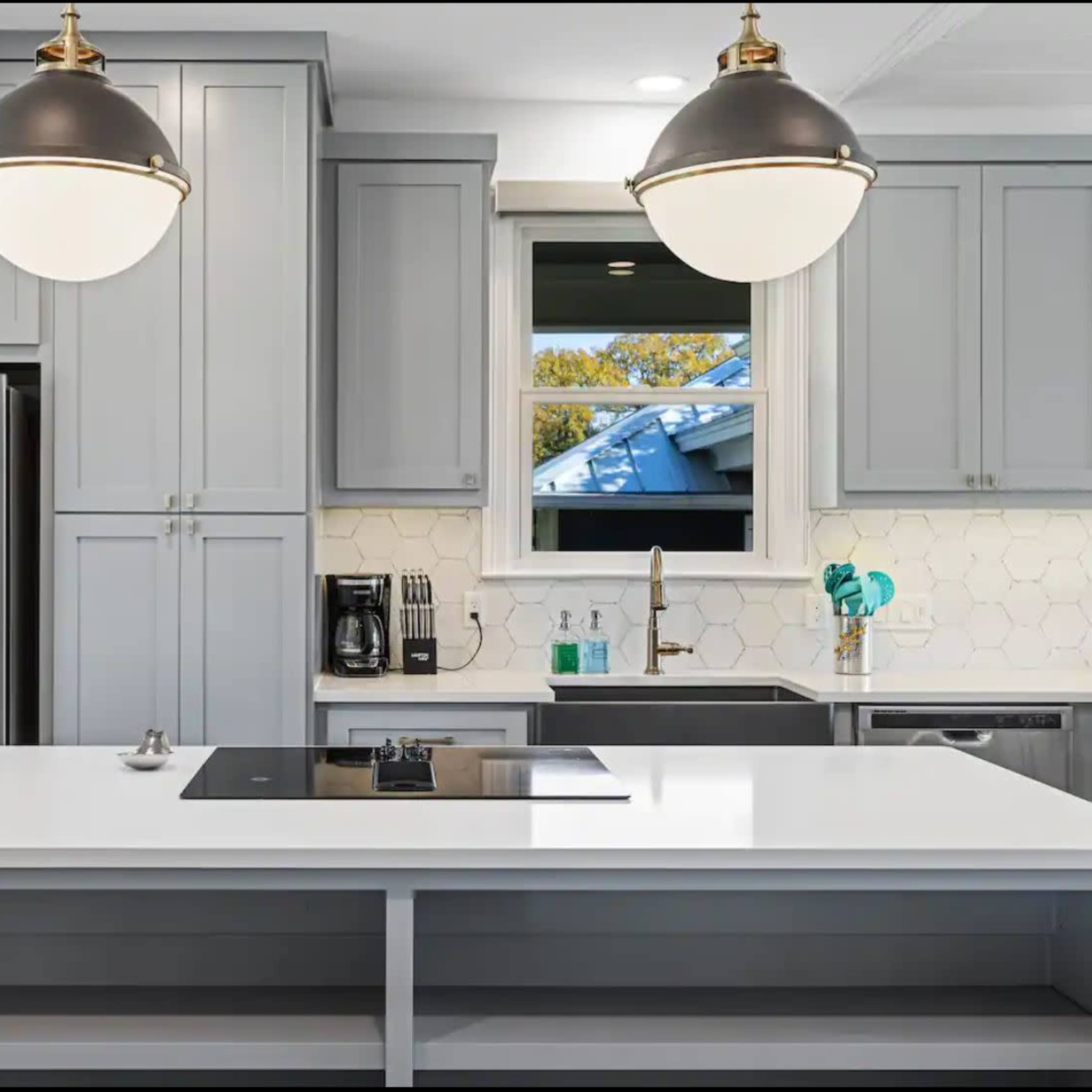 A modern kitchen features gray cabinetry, a large white island with a cooktop, and stainless steel appliances.