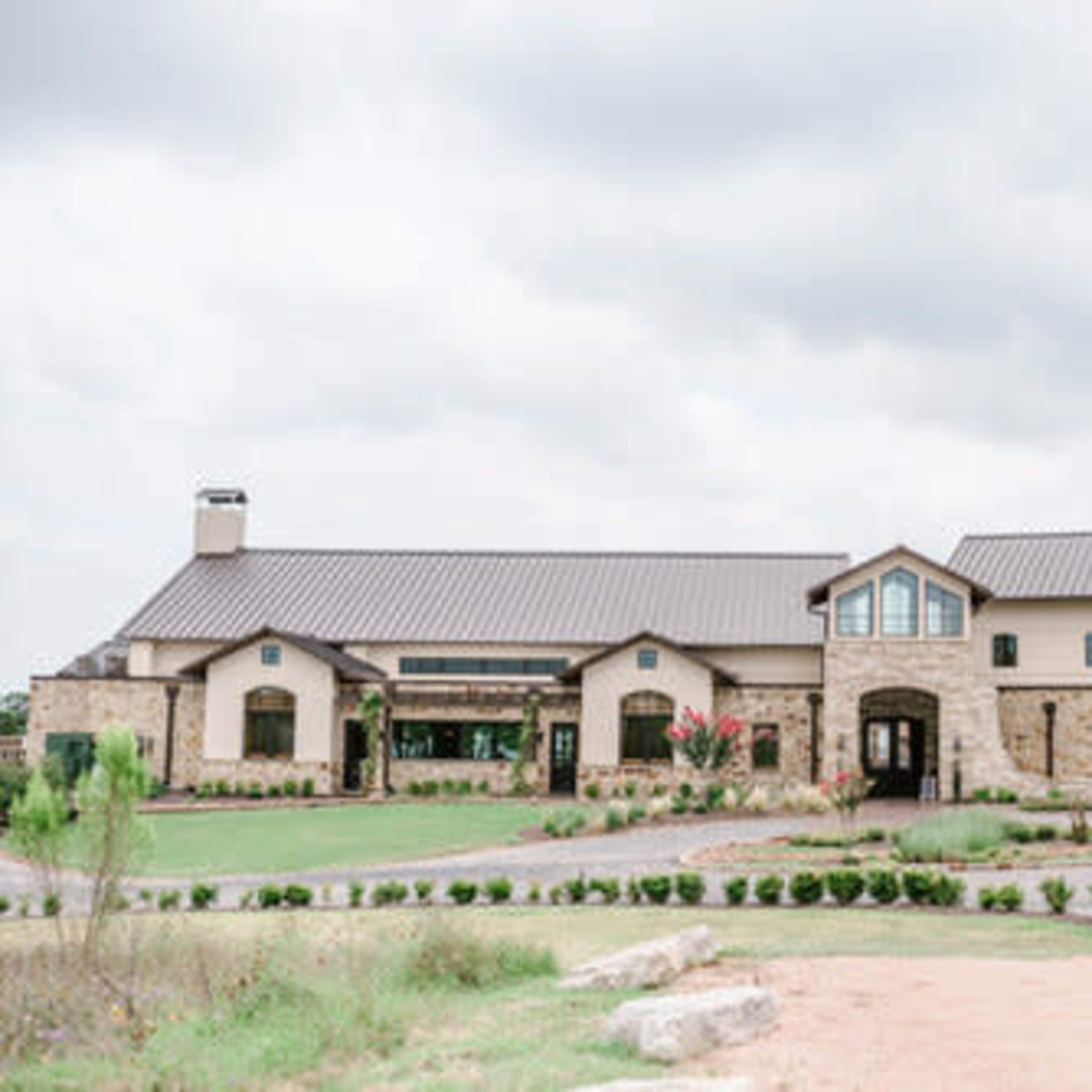 A large two-story building with a combination of stone and stucco exterior, featuring multiple windows and a landscaped front yard.