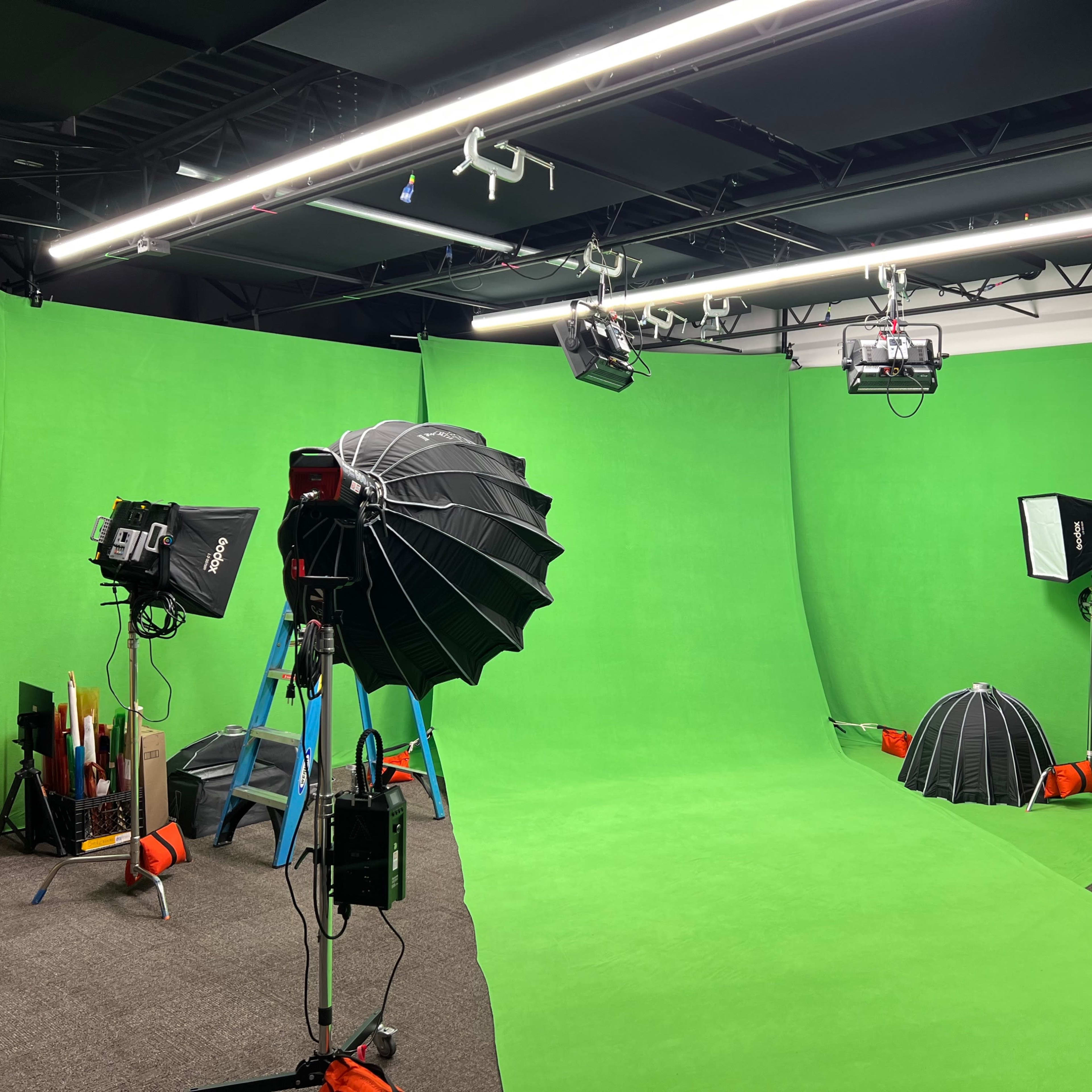 A film studio setup with green backgrounds, lighting equipment, and a ladder positioned in the center.