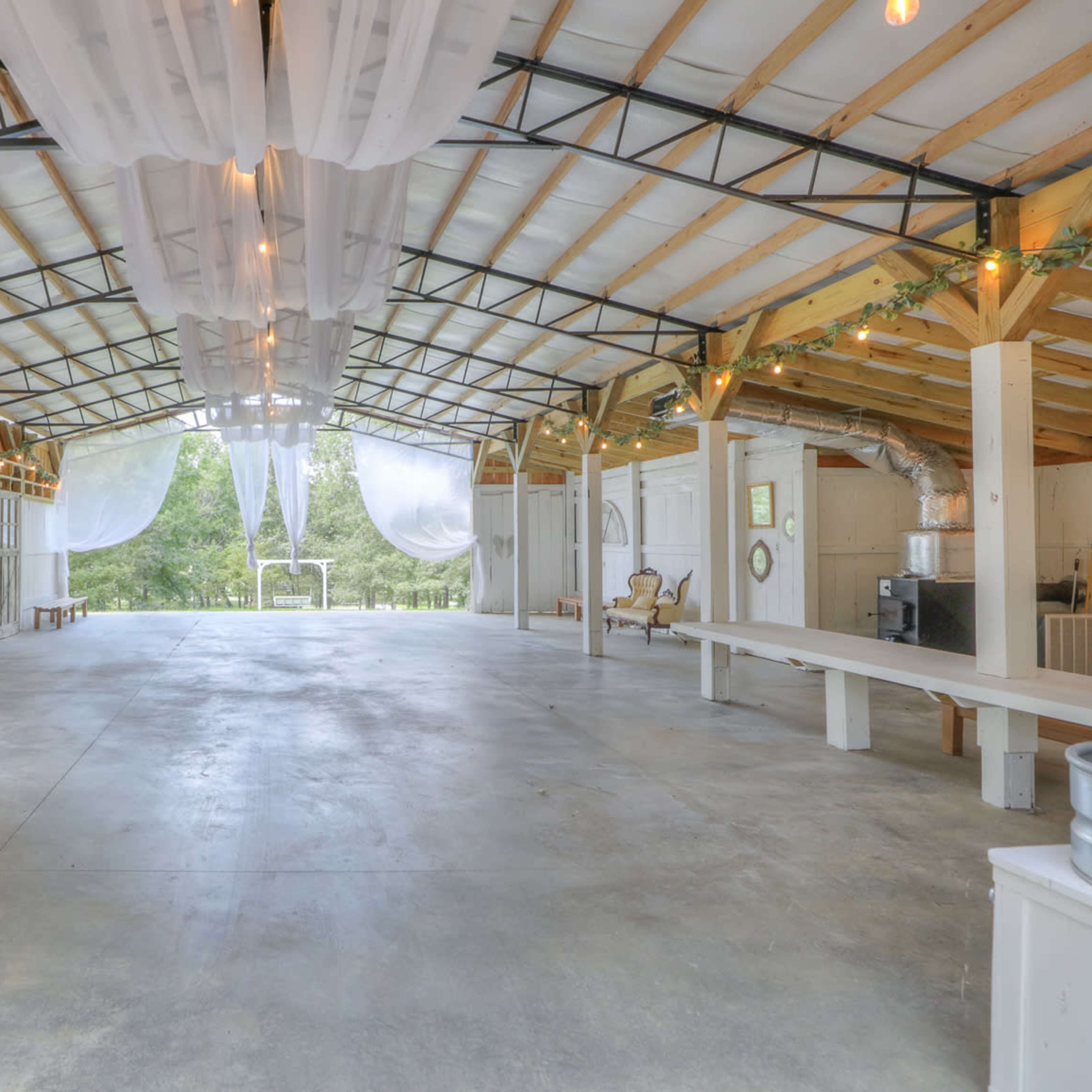 A spacious indoor venue with a high ceiling, exposed wooden beams, and decorative drapery, featuring a wooden bar and seating areas.