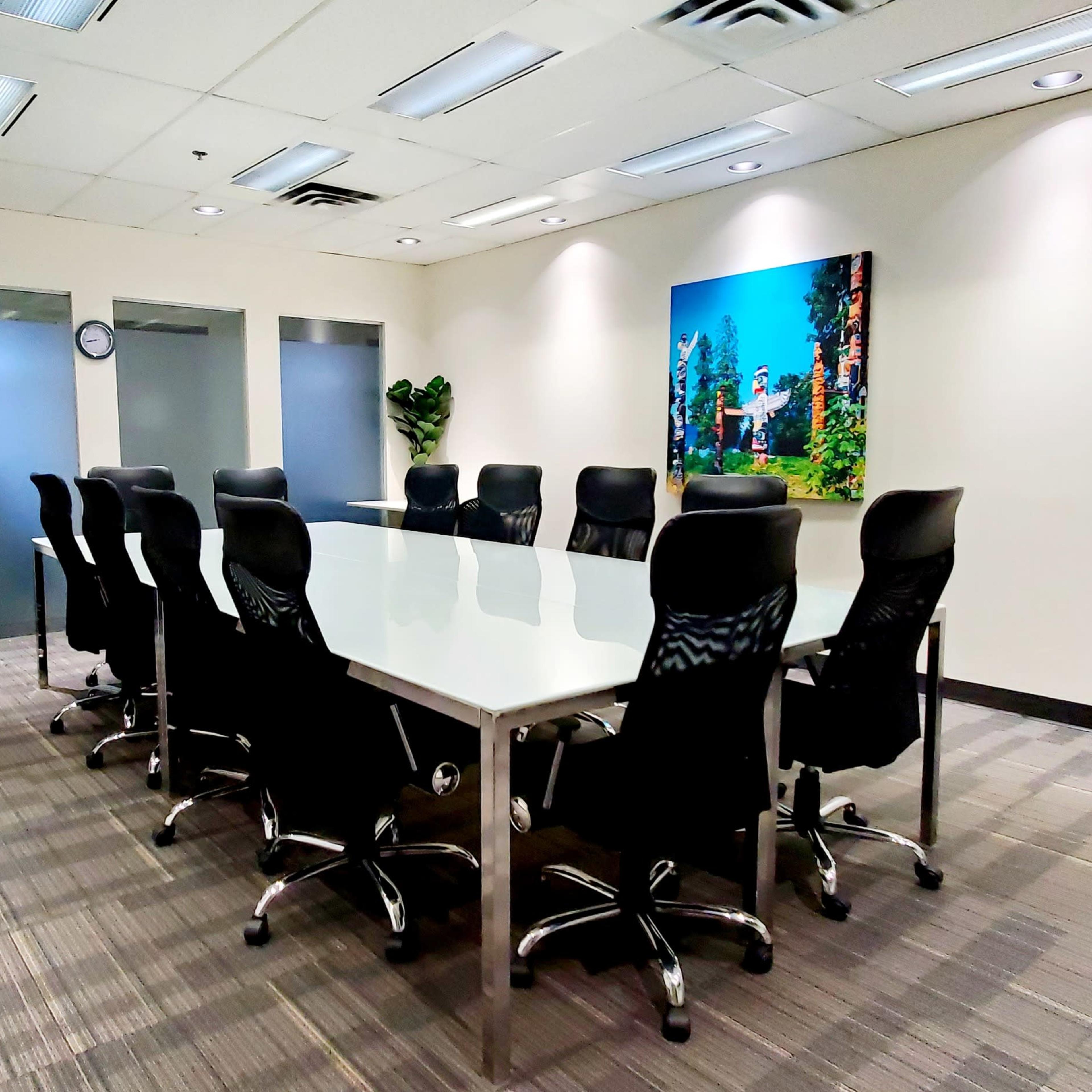A modern conference room features a long table surrounded by ergonomic chairs, with a large wall art piece and plants decorating the space.