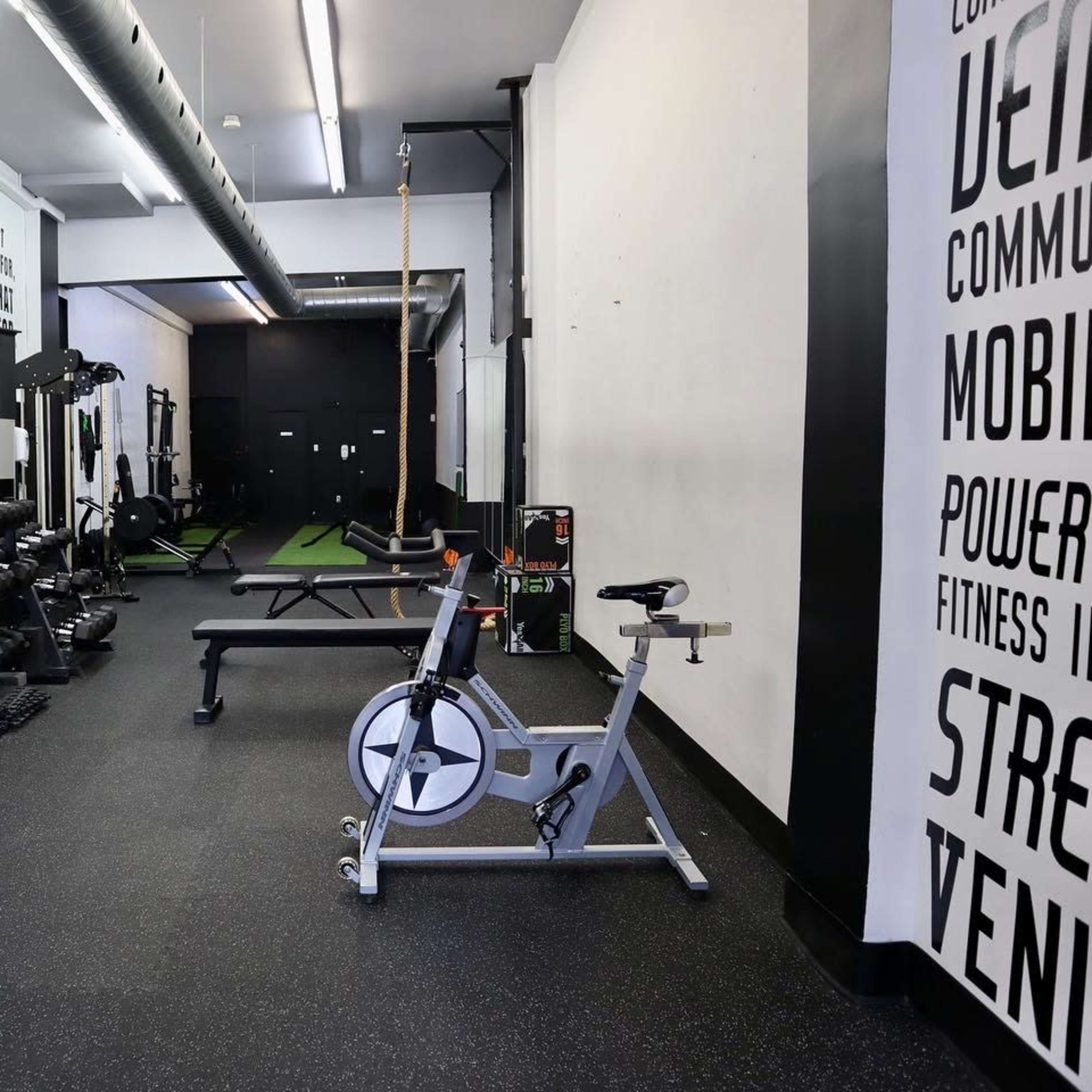 A modern gym with exercise equipment, including dumbbells, a weight bench, and a stationary bike, set against a minimalist black and white backdrop.
