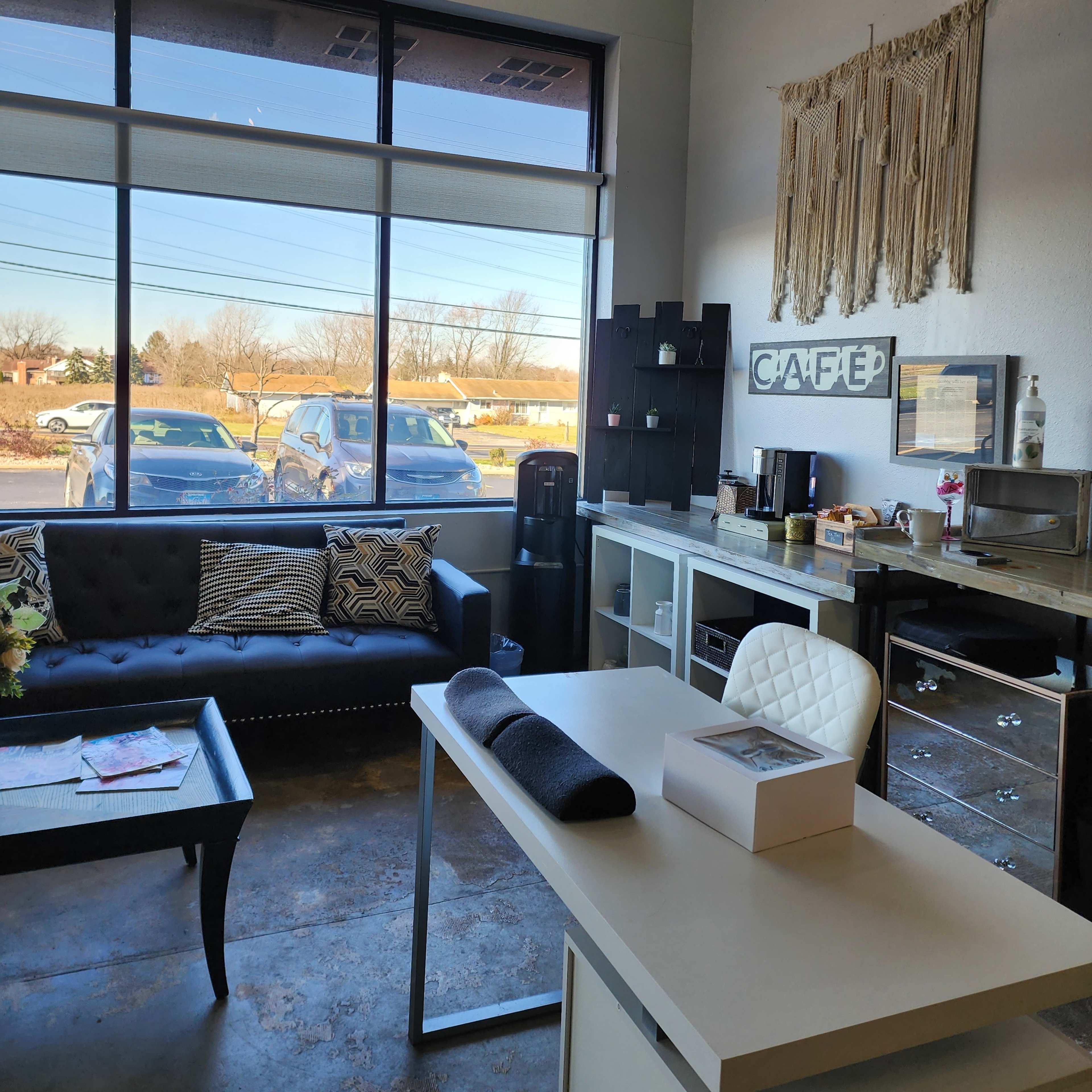 A modern cafe interior with a seating area, a desk, and large windows displaying parked cars outside.