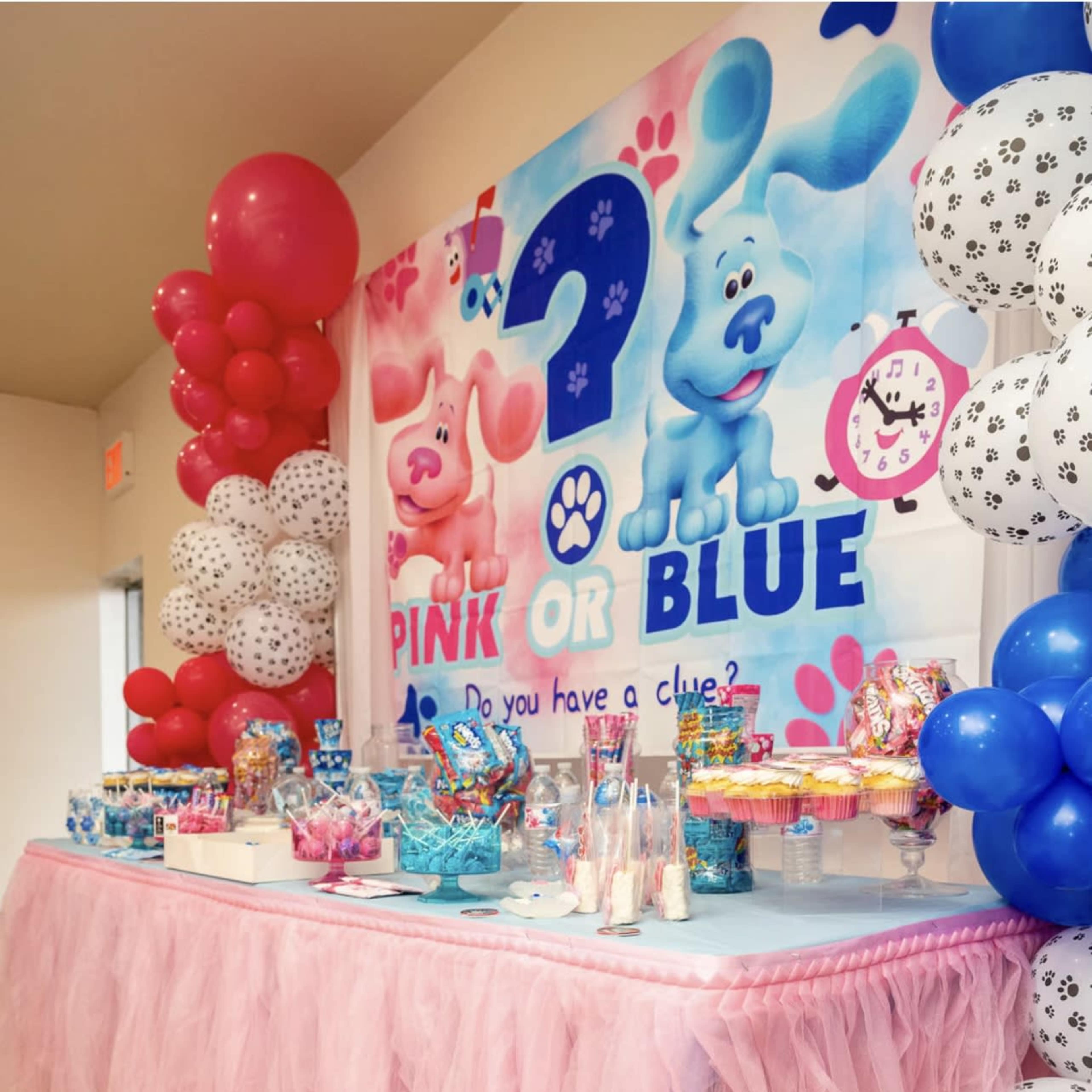A decorated table with pink tulle, surrounded by balloons, features a colorful dessert spread for a "Pink or Blue" themed party.