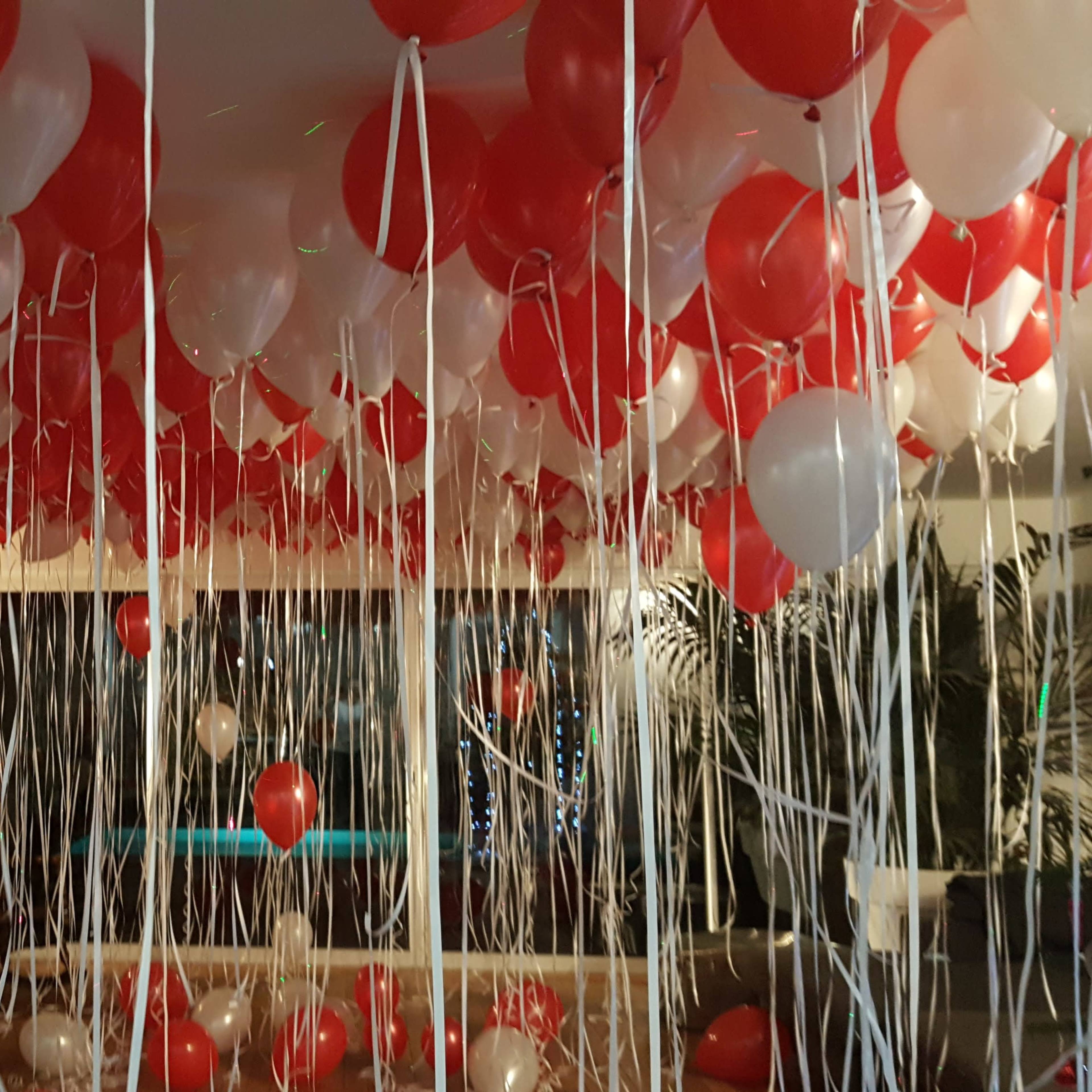 The room is filled with red and white balloons hanging from the ceiling, creating a festive atmosphere.