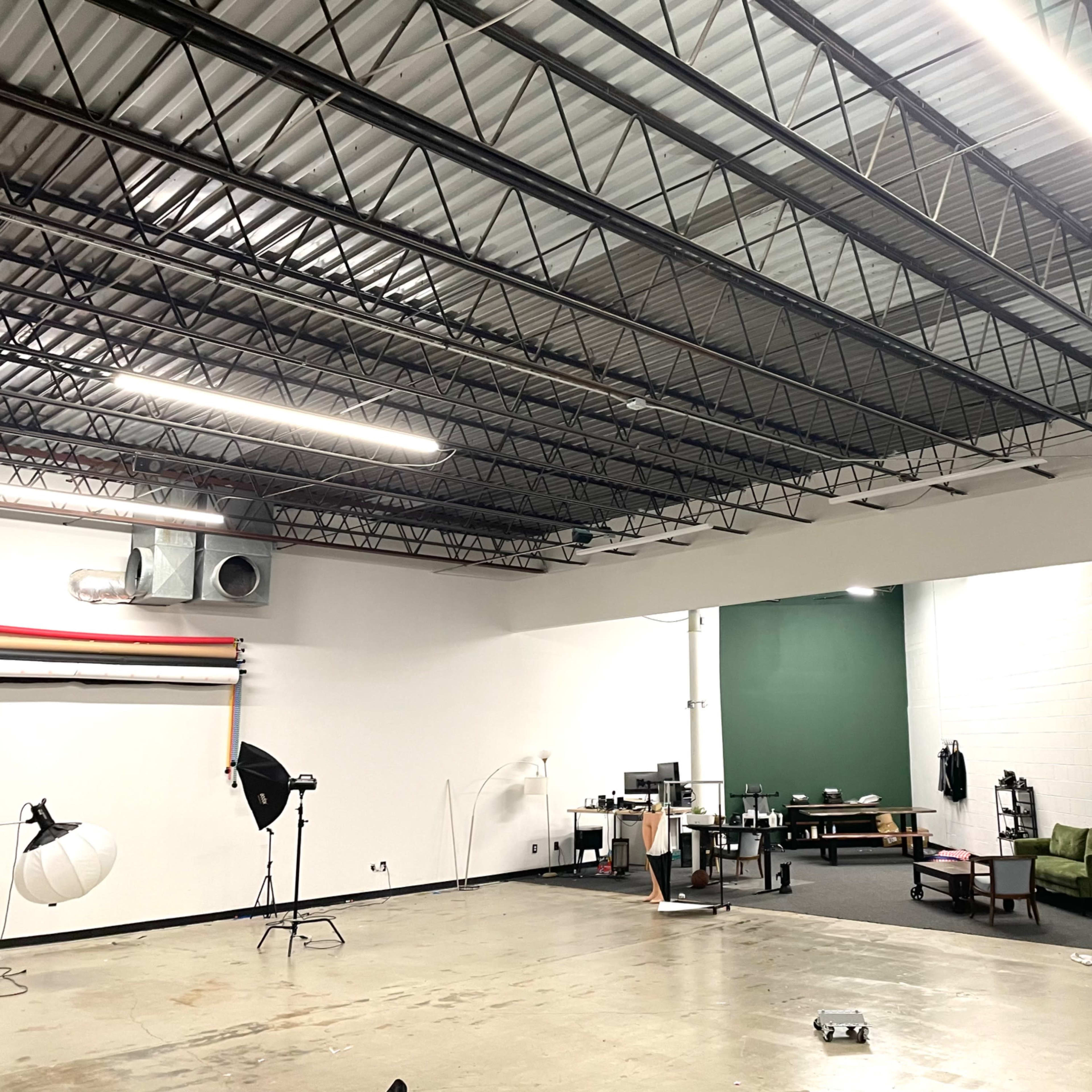 A spacious room with high ceilings featuring divided areas for a photography studio and a lounge, equipped with various furniture and equipment.